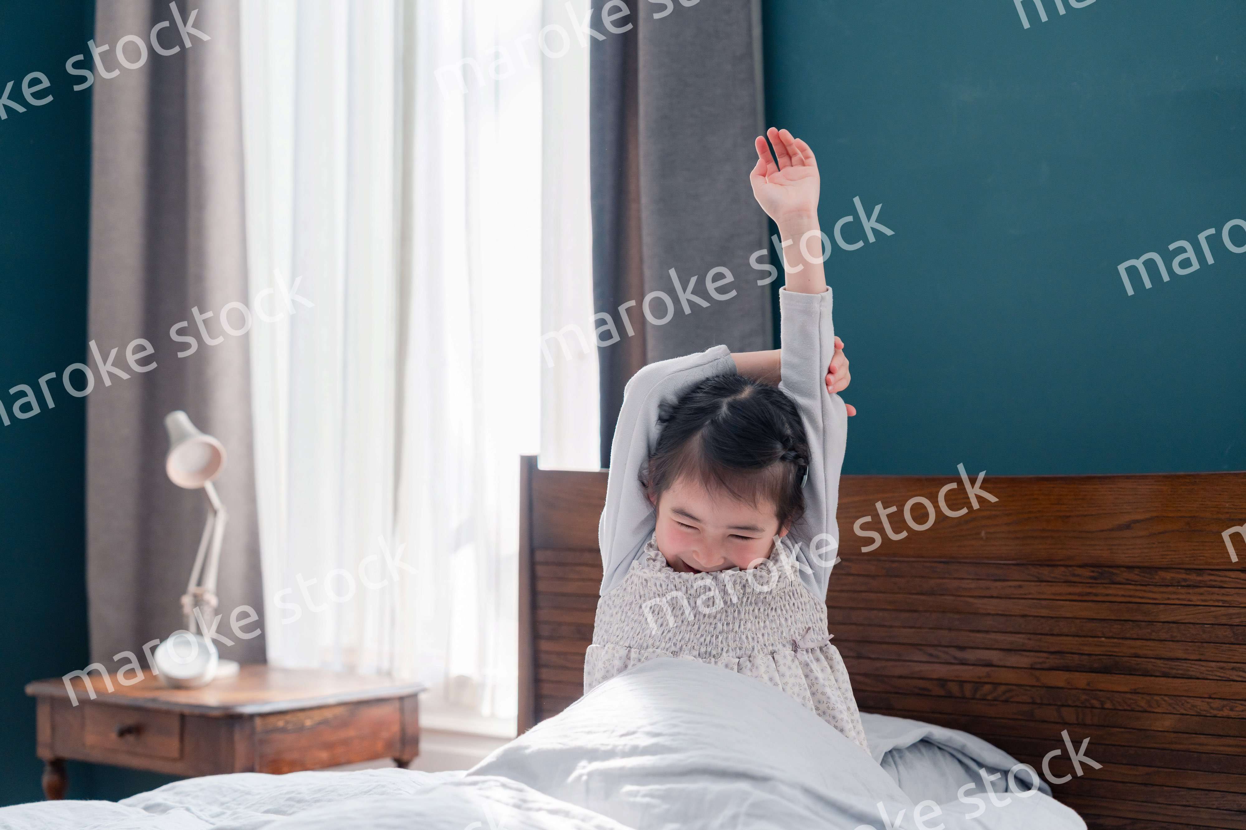 朝ベッドで目覚めて伸びをする小さな女の子