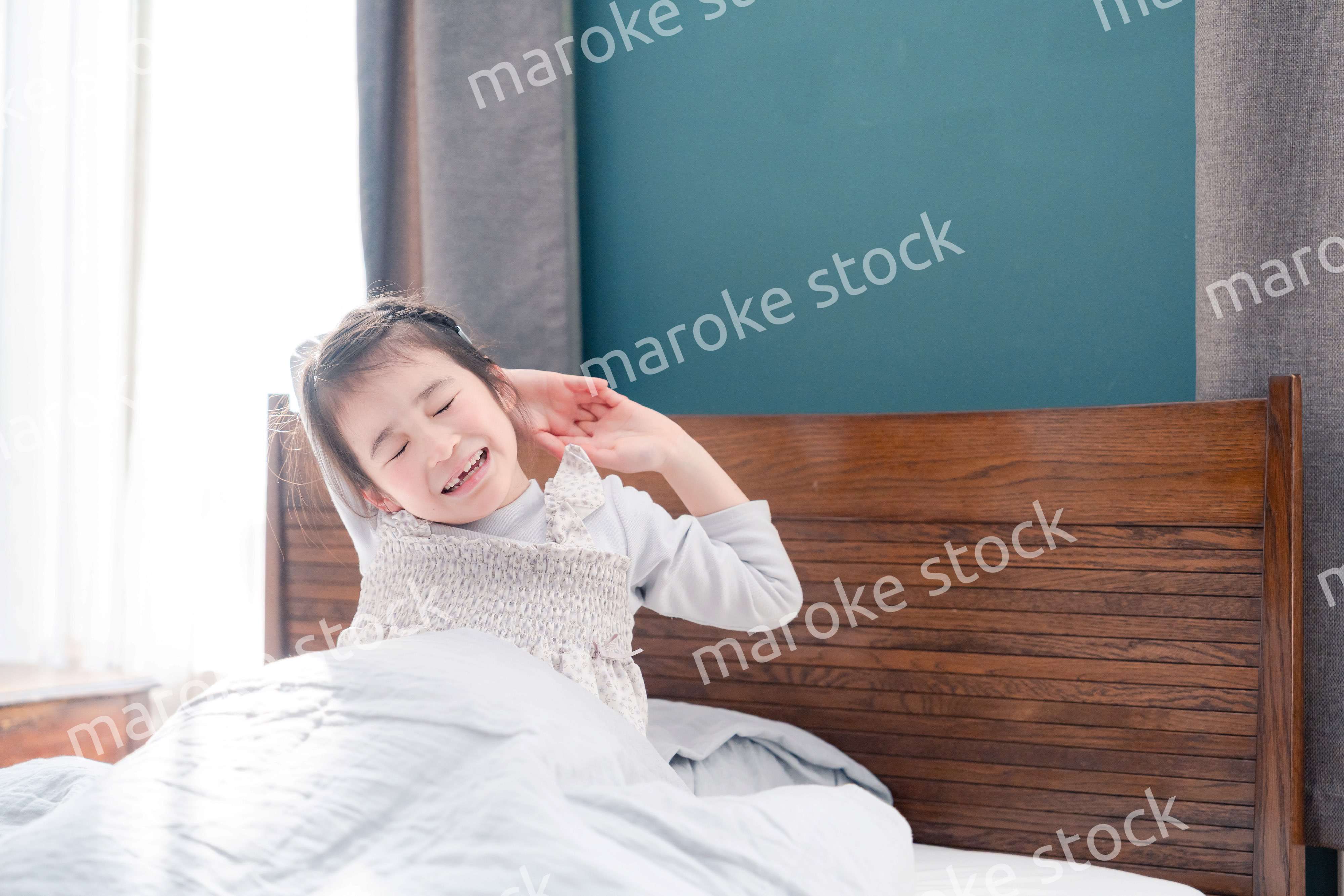 朝ベッドで目覚めて伸びをする小さな女の子