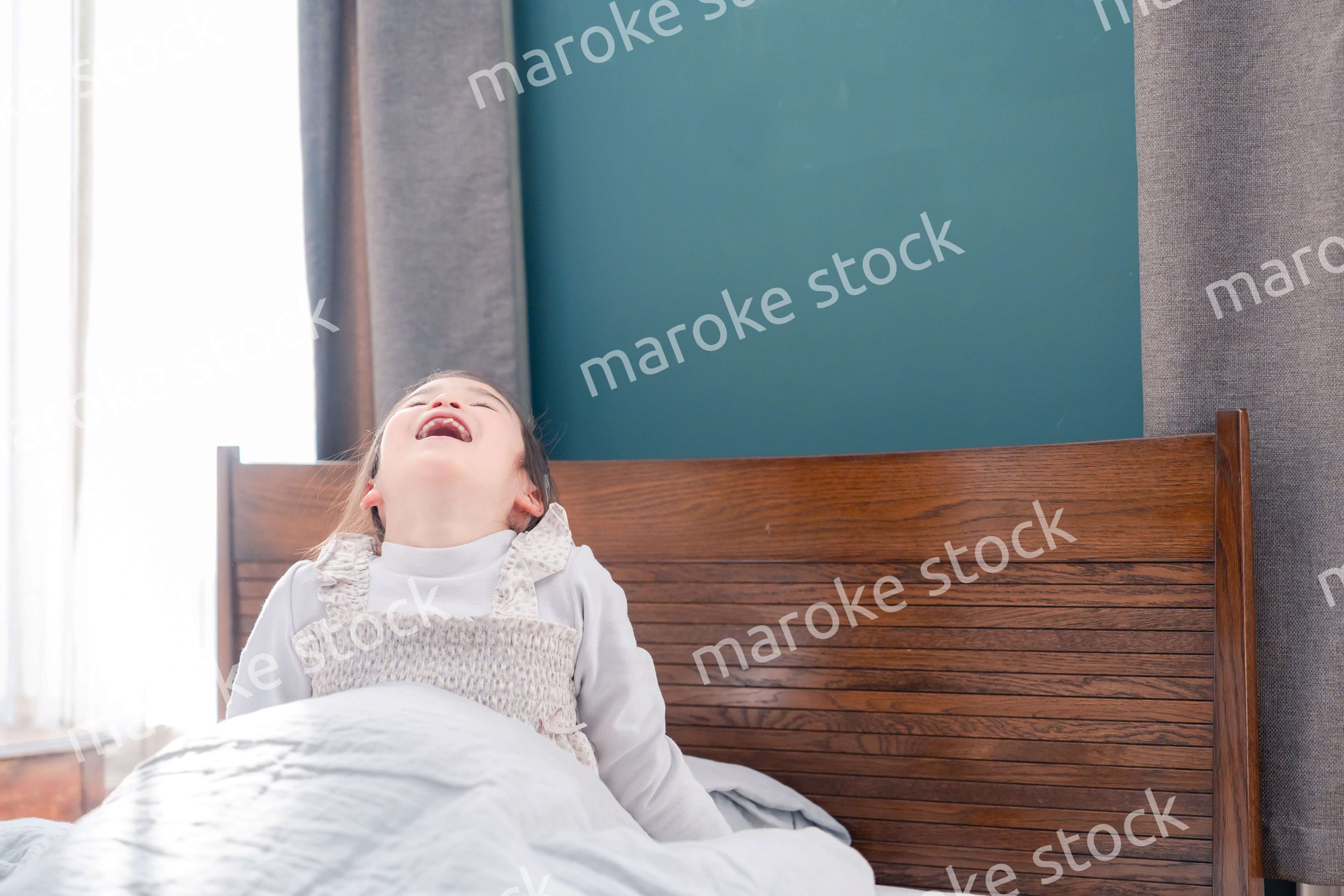 朝ベッドで目覚めて伸びをする小さな女の子