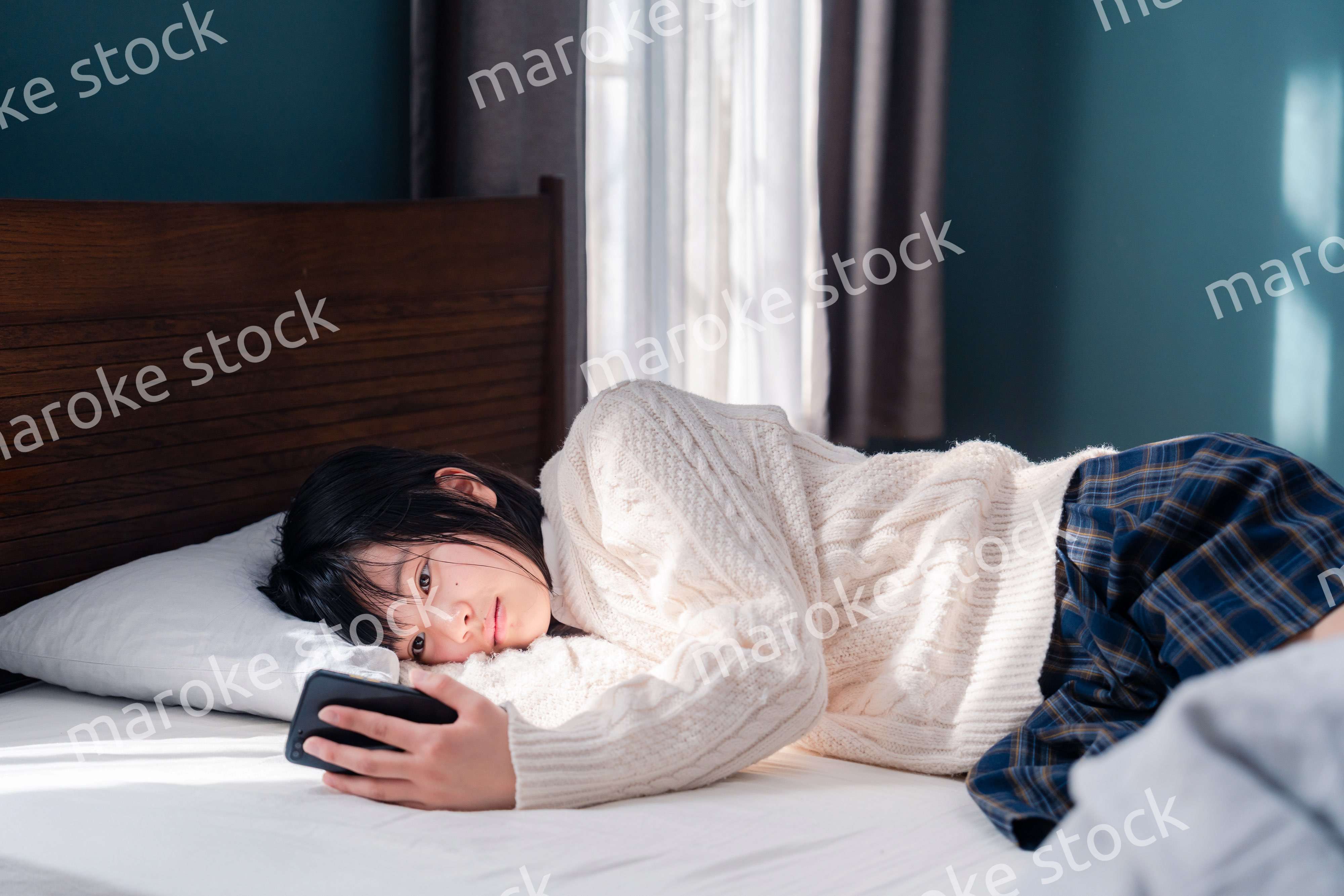 ベッドに寝転がってスマホを使う思春期の少女