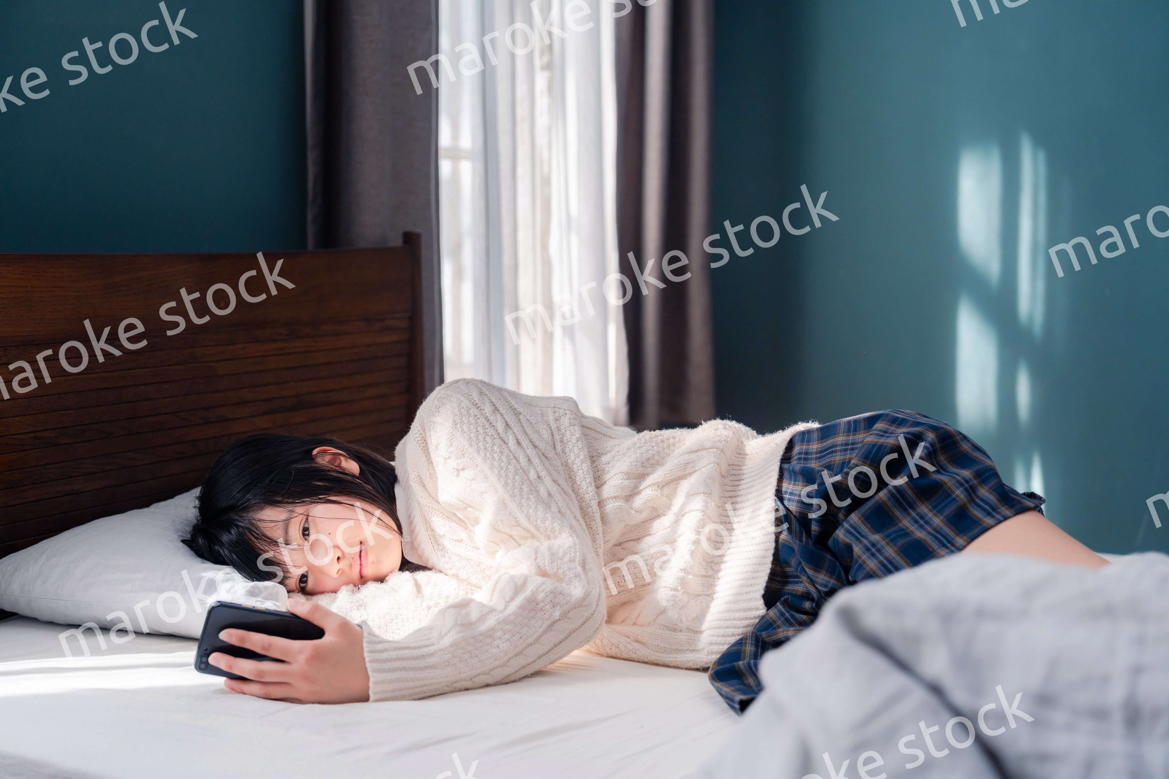 ベッドに寝転がってスマホを使う思春期の少女