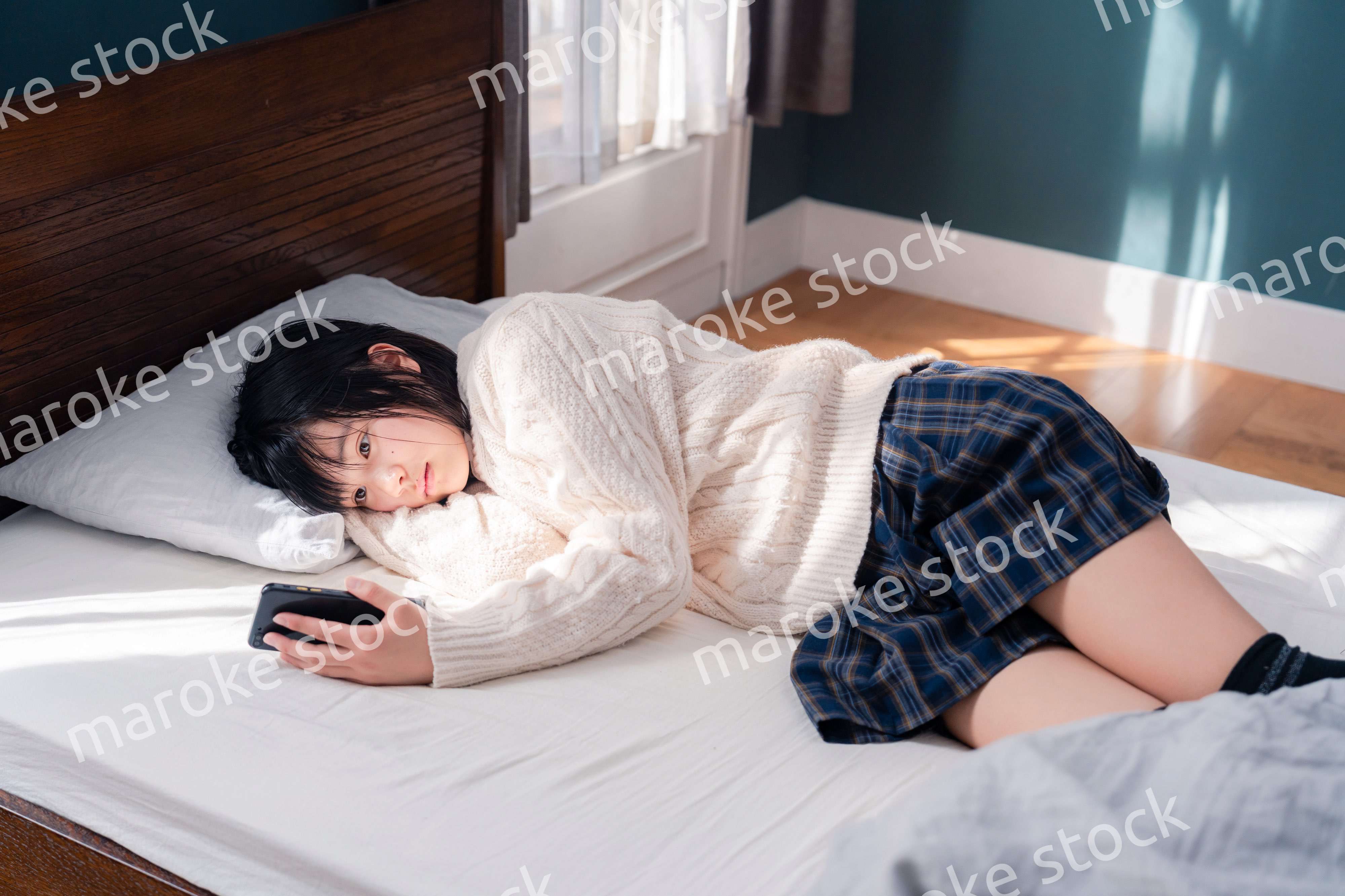 ベッドに寝転がってスマホを使う思春期の少女