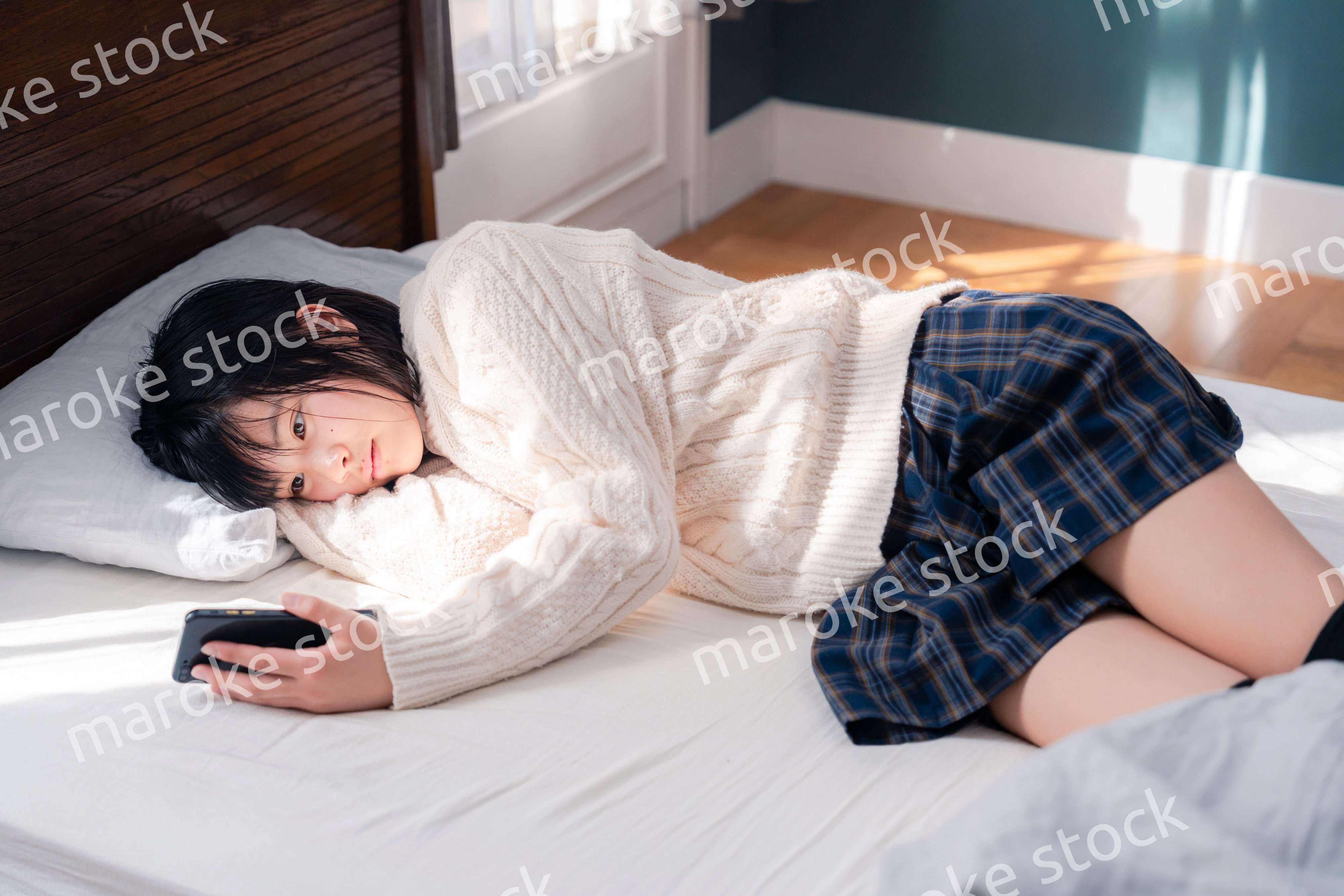 ベッドに寝転がってスマホを使う思春期の少女