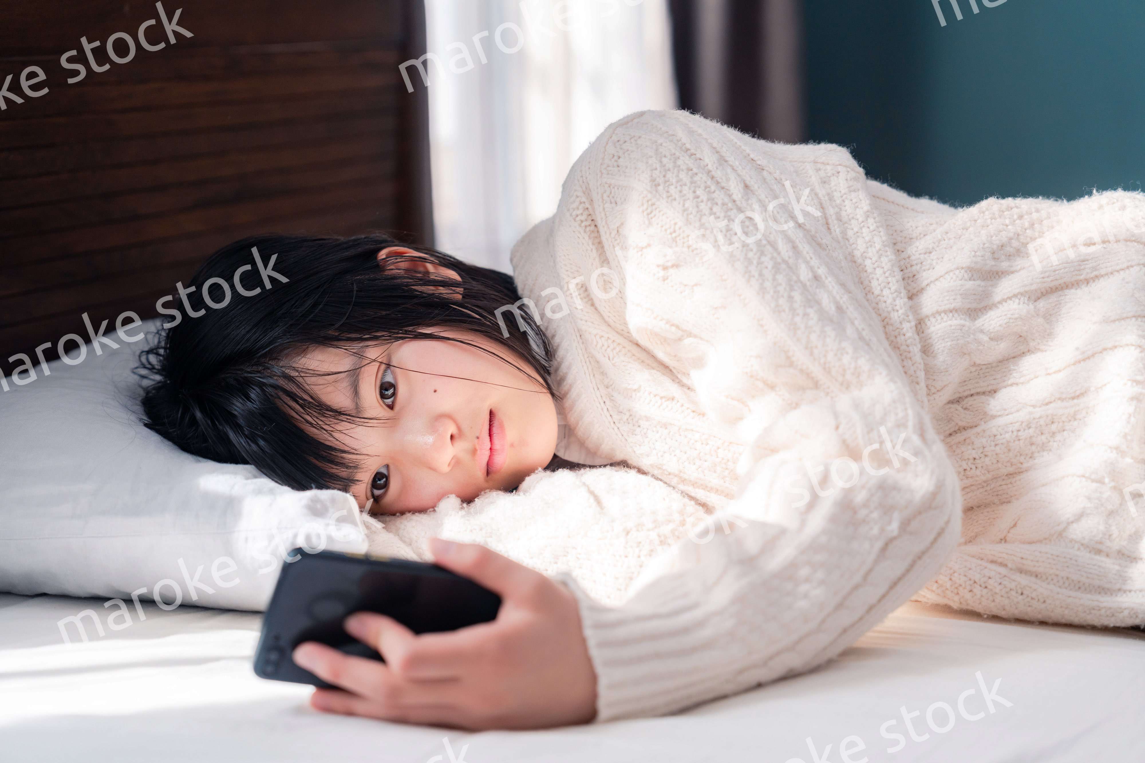 ベッドに寝転がってスマホを使う思春期の少女