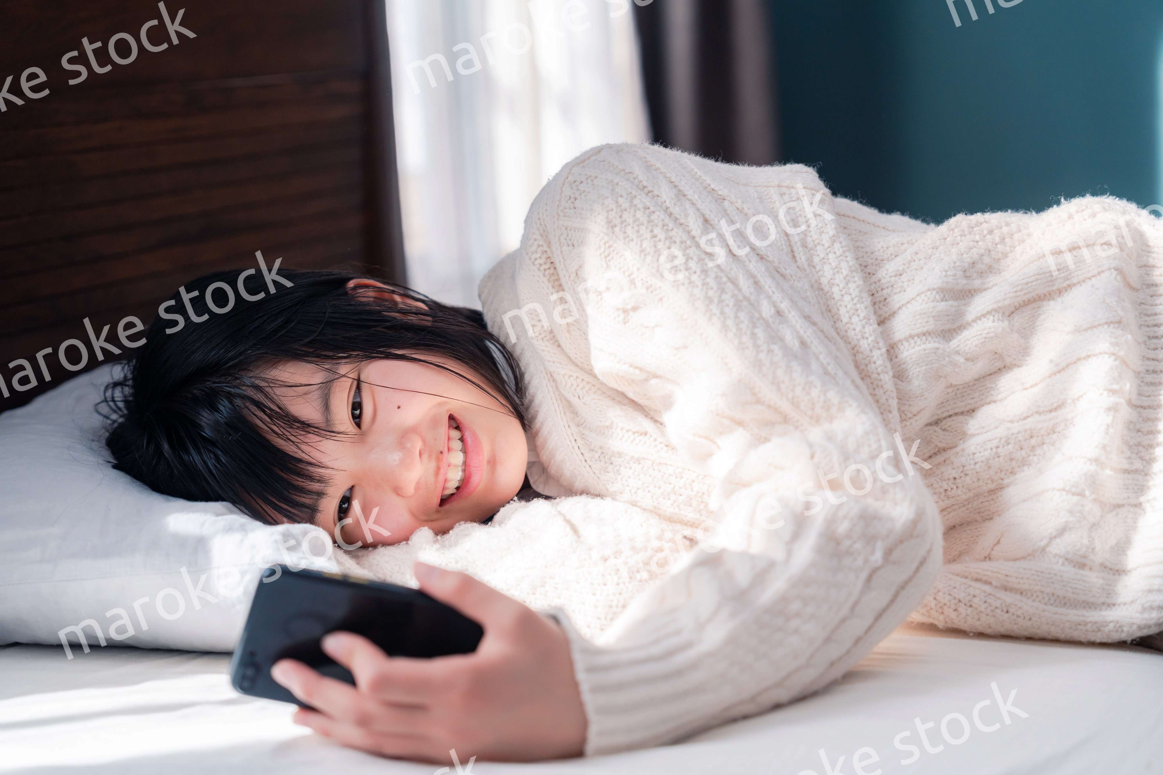 ベッドに寝転がってスマホを使う思春期の少女