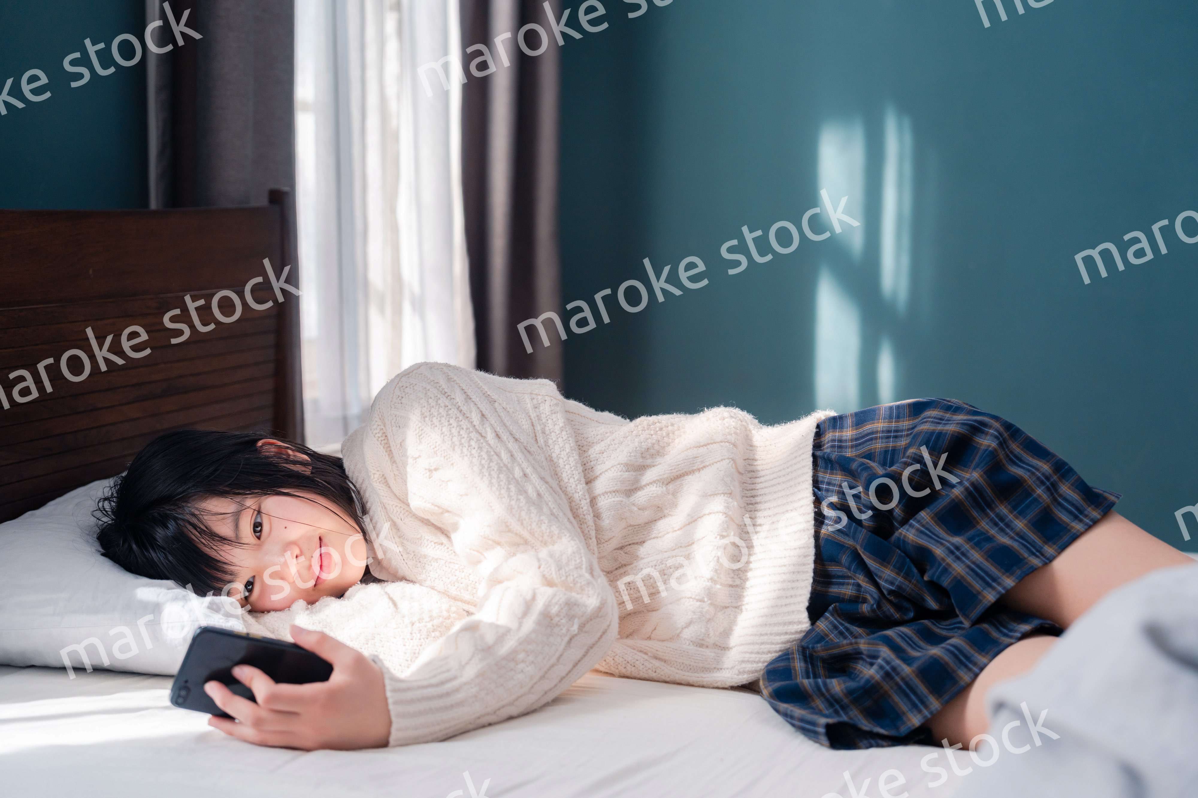 ベッドに寝転がってスマホを使う思春期の少女