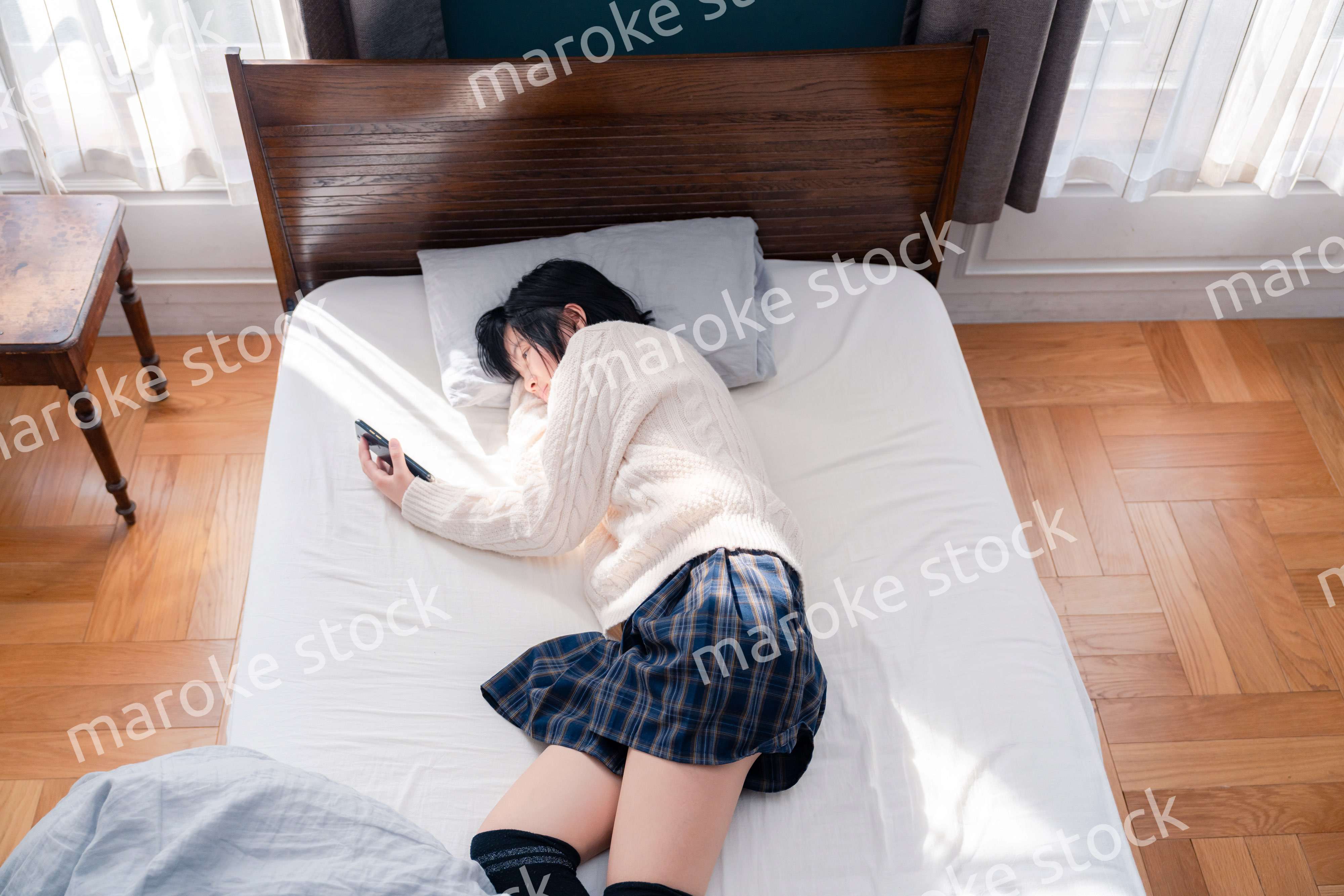 ベッドに寝転がってスマホを使う思春期の少女