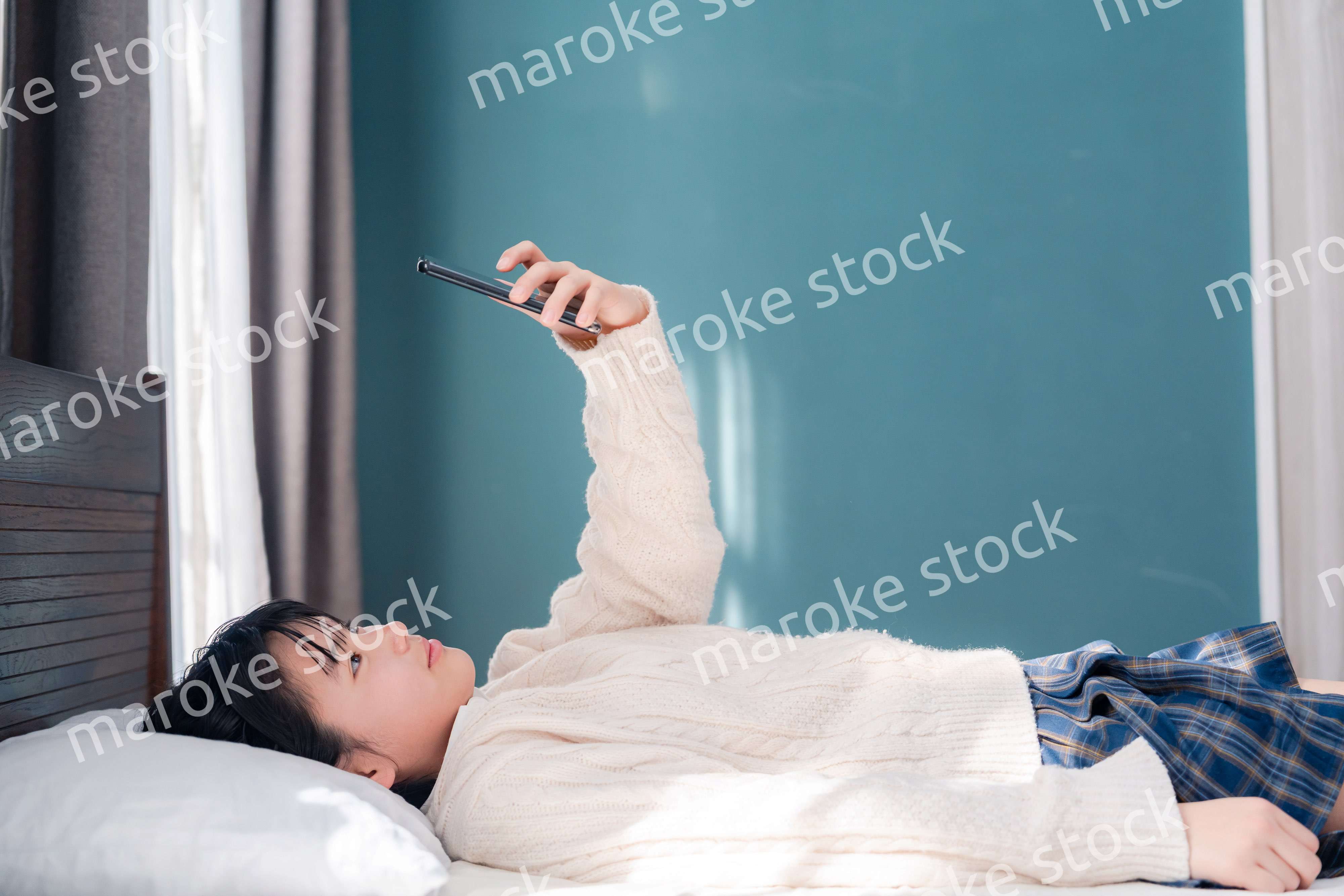 ベッドに寝転がってスマホを使う思春期の少女