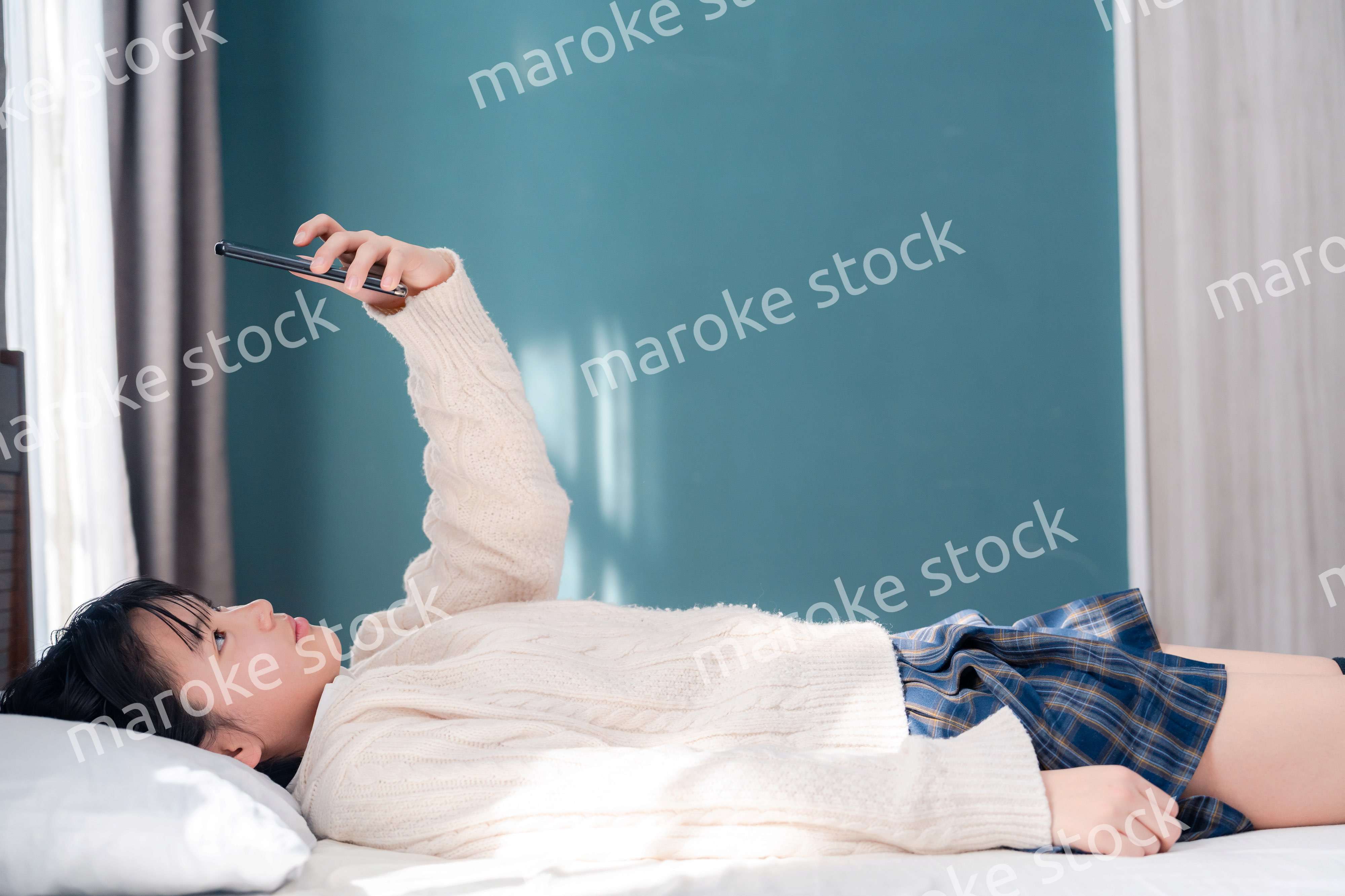 ベッドに寝転がってスマホを使う思春期の少女