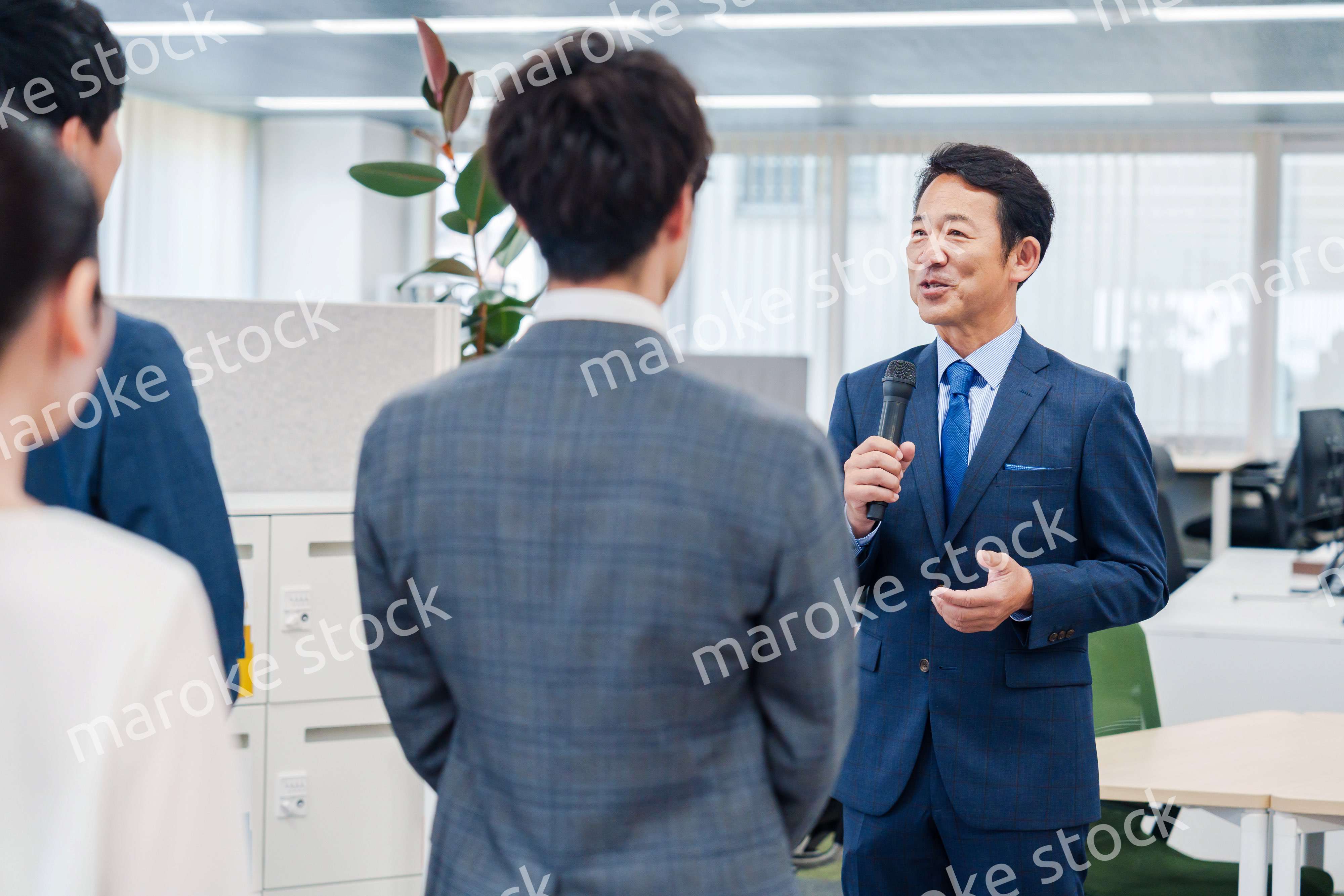 オフィスでの朝礼で挨拶をする管理職の男性