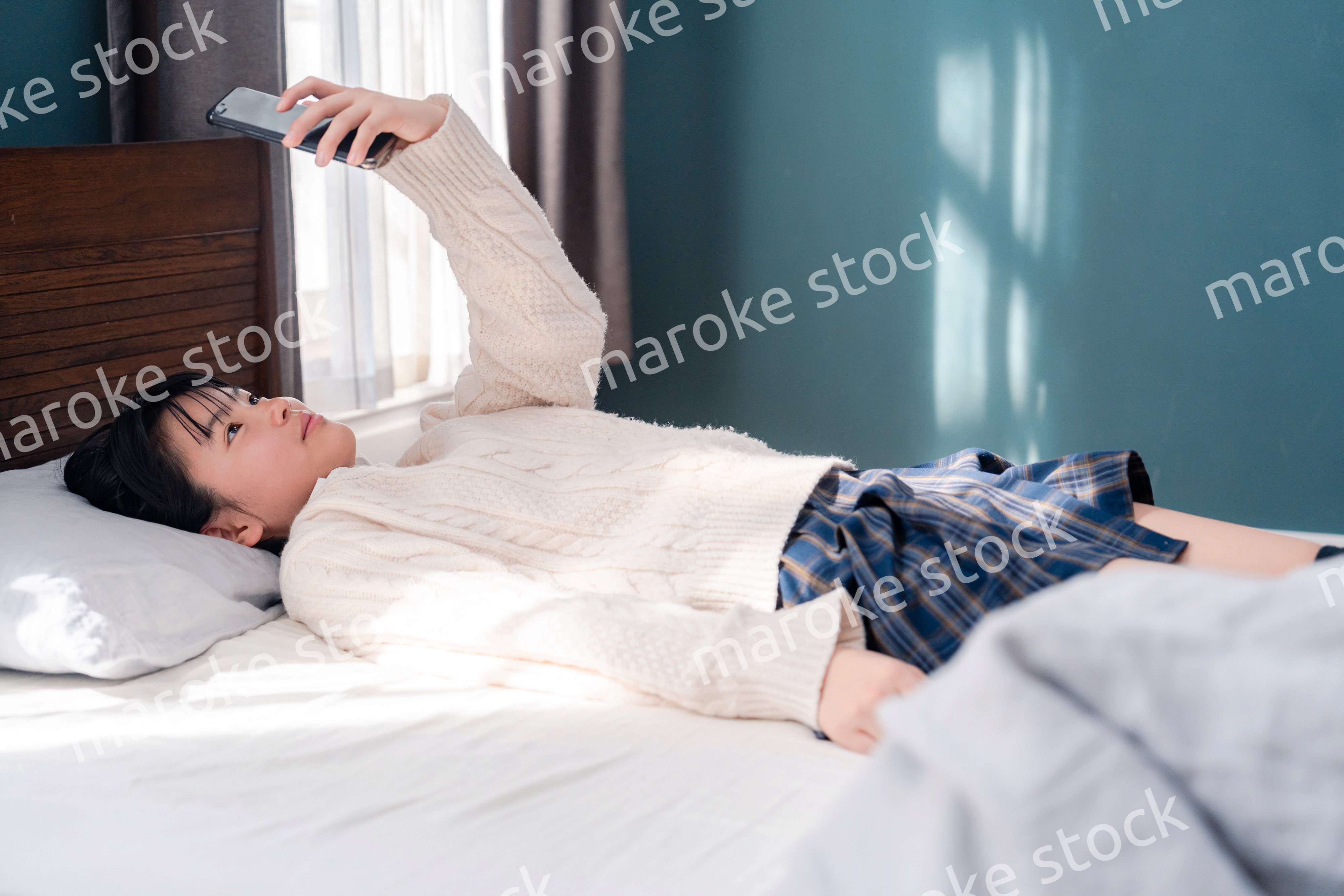 ベッドに寝転がってスマホを使う思春期の少女