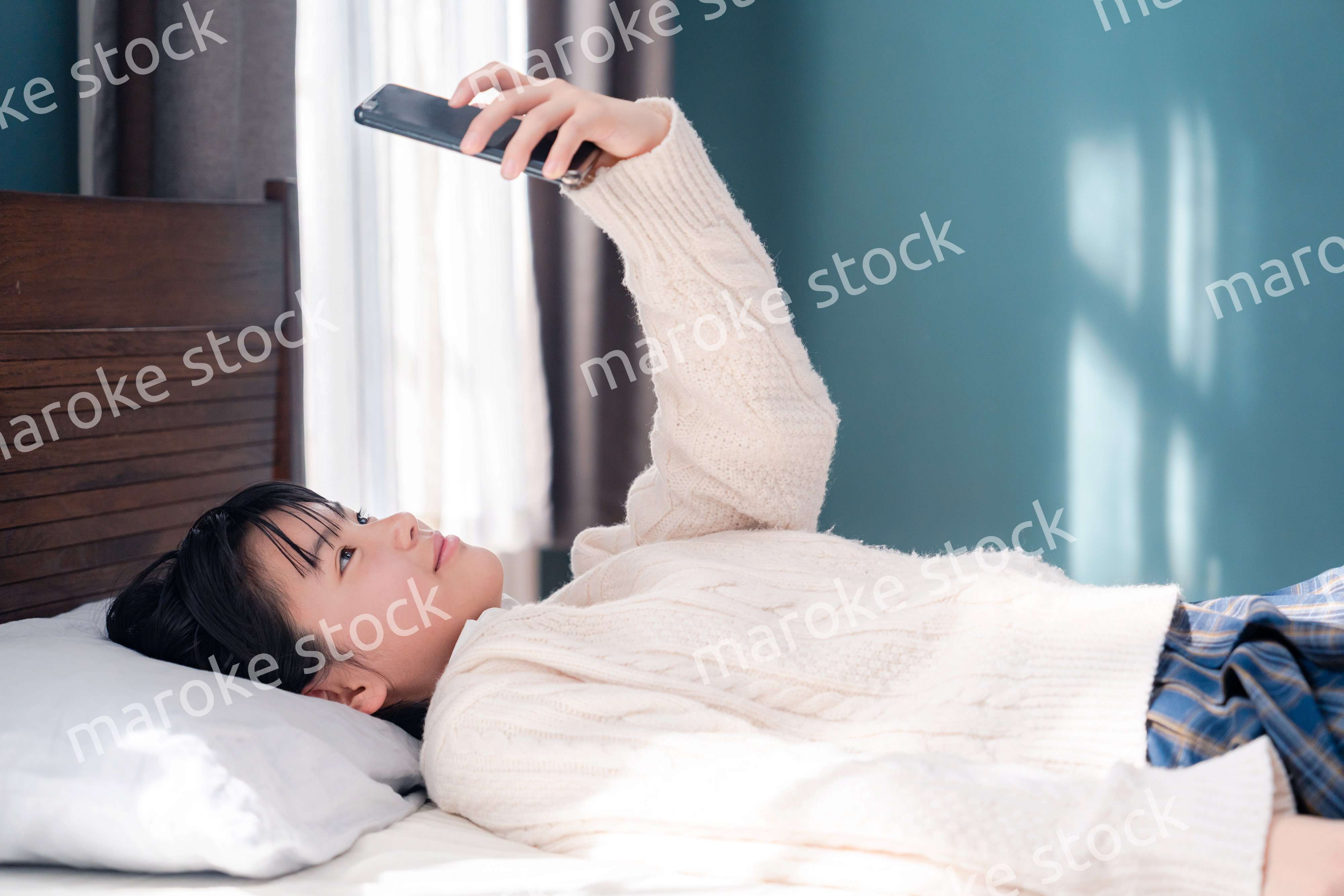 ベッドに寝転がってスマホを使う思春期の少女