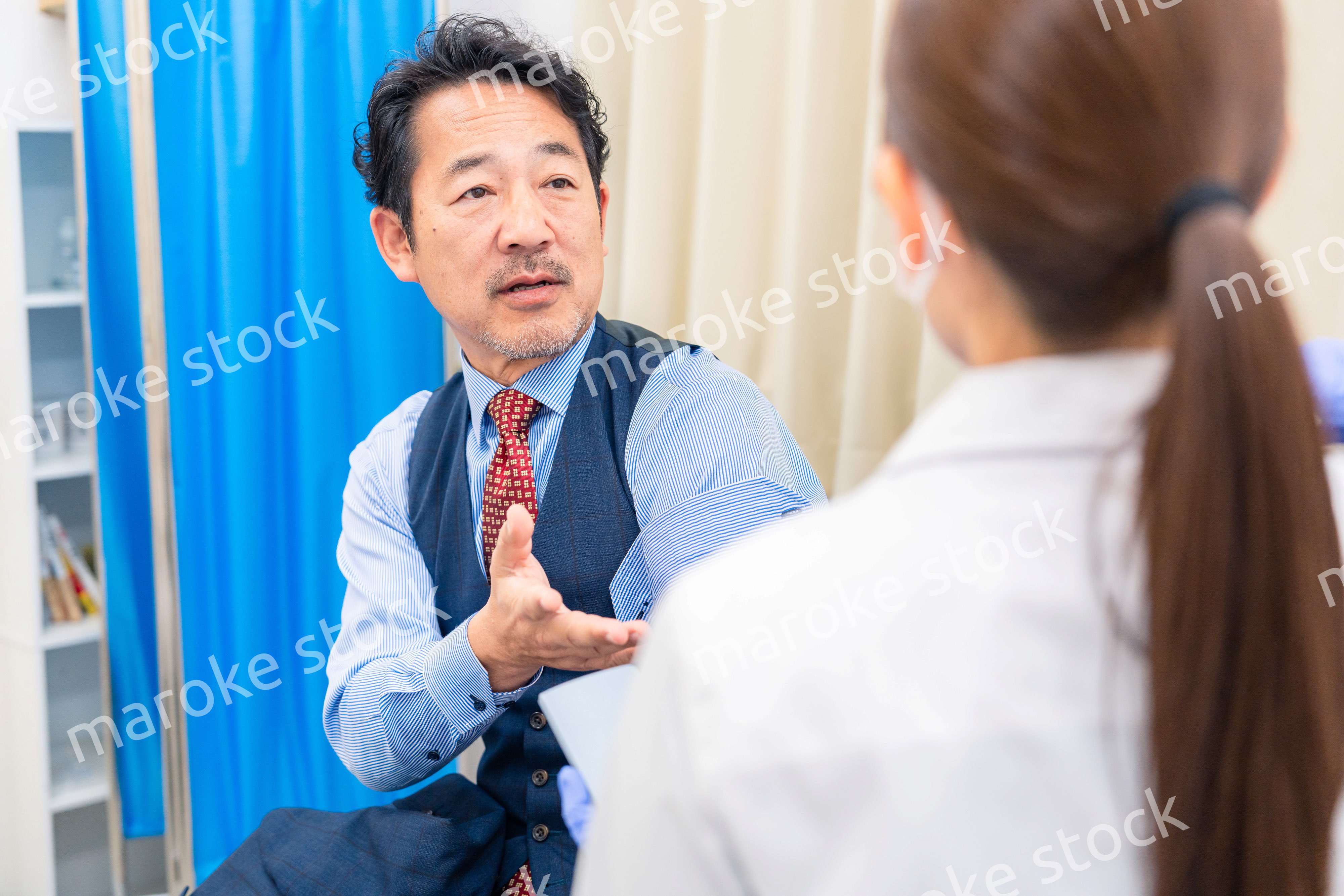 病院で男性患者の問診をする女性医師