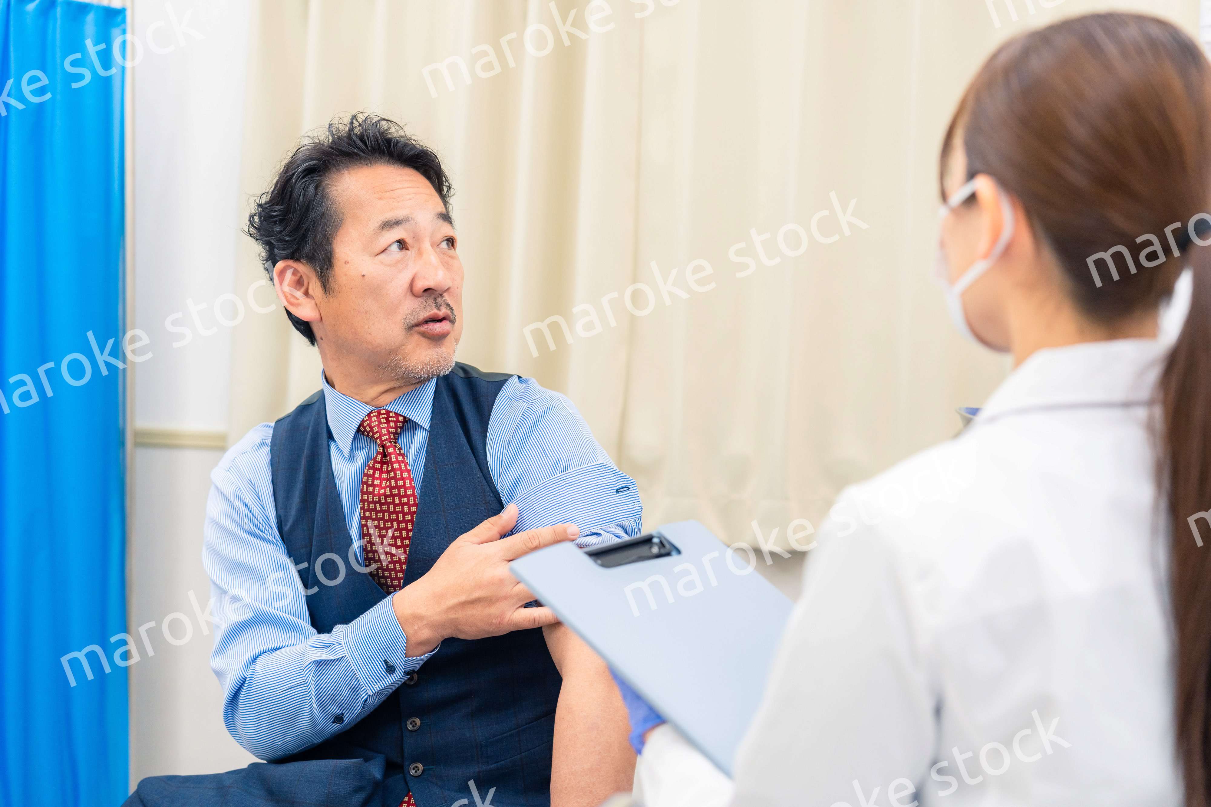 病院で男性患者の問診をする女性医師