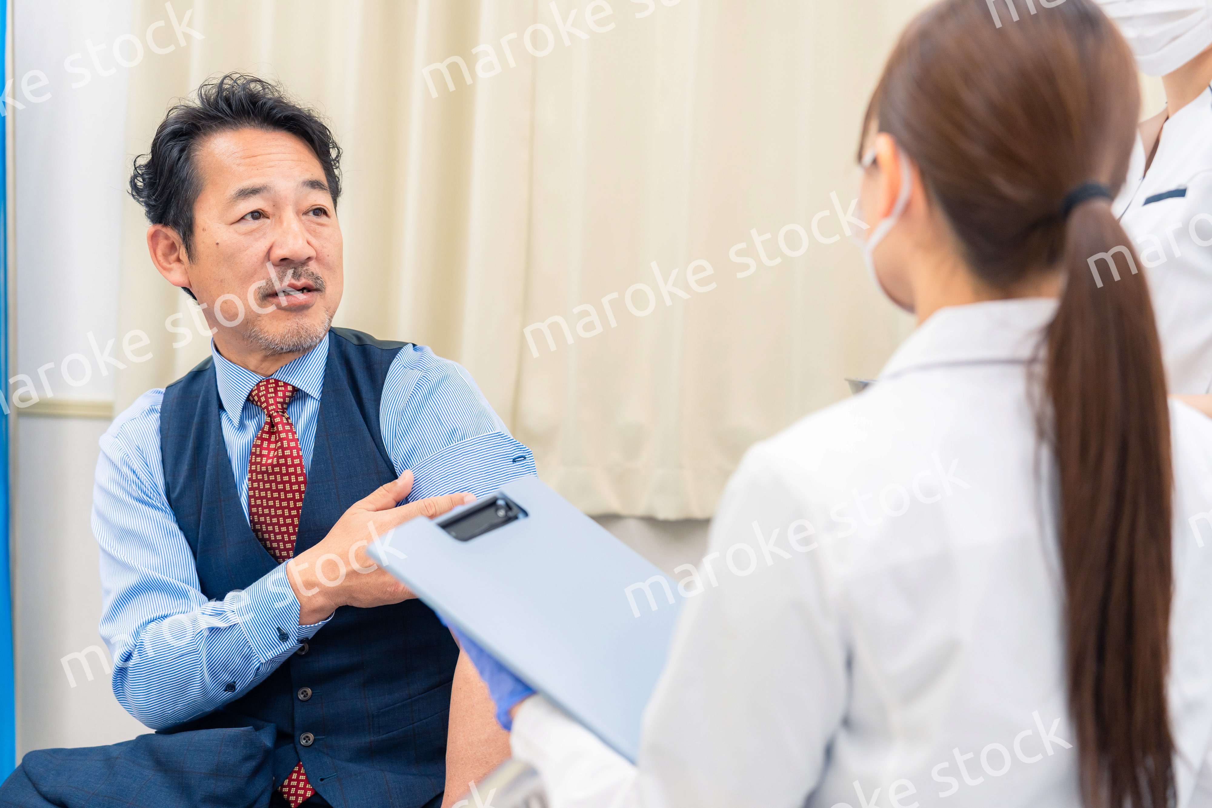 病院で男性患者の問診をする女性医師