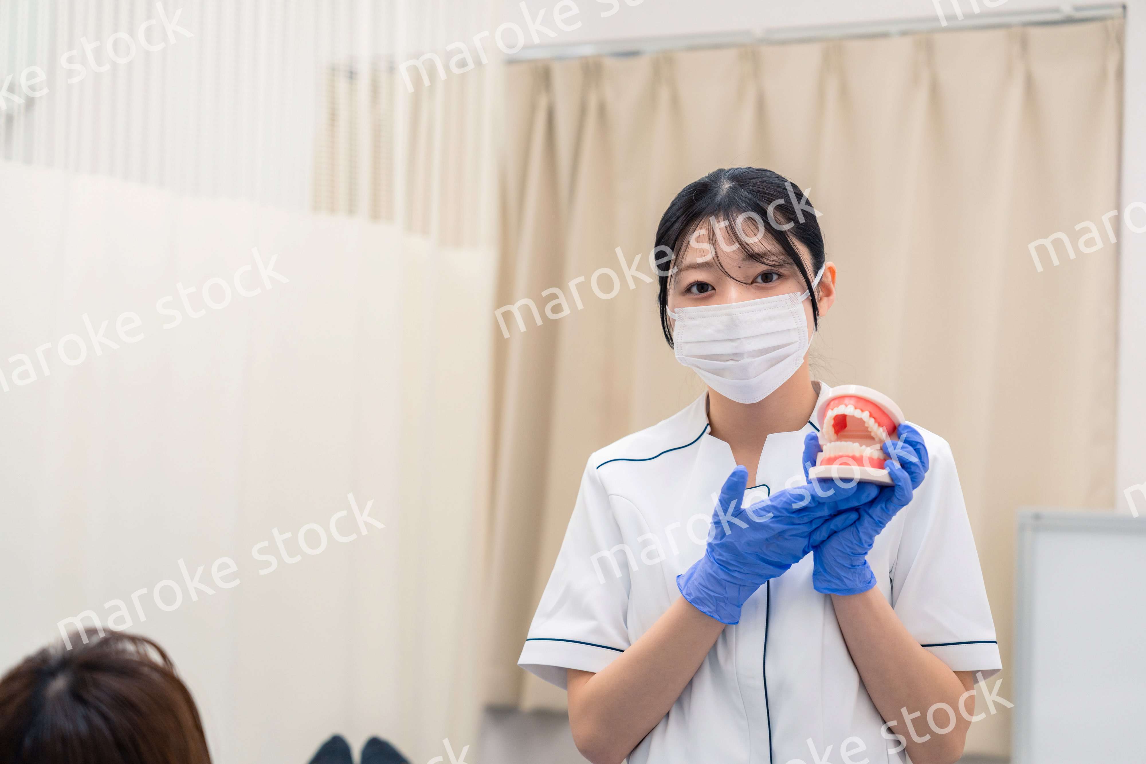歯の模型を使って患者に説明をする歯科助手の女性