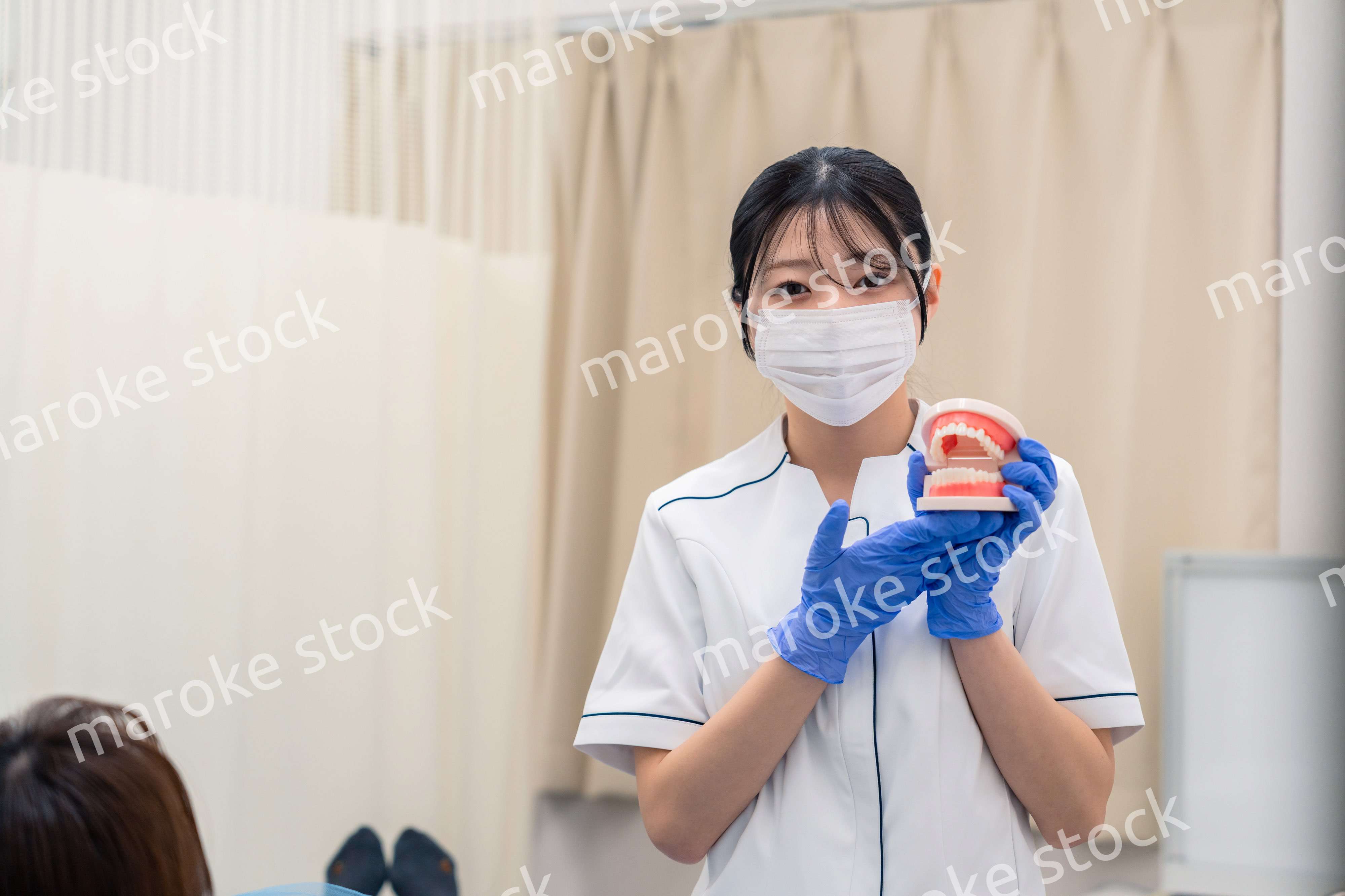 歯の模型を使って患者に説明をする歯科助手の女性