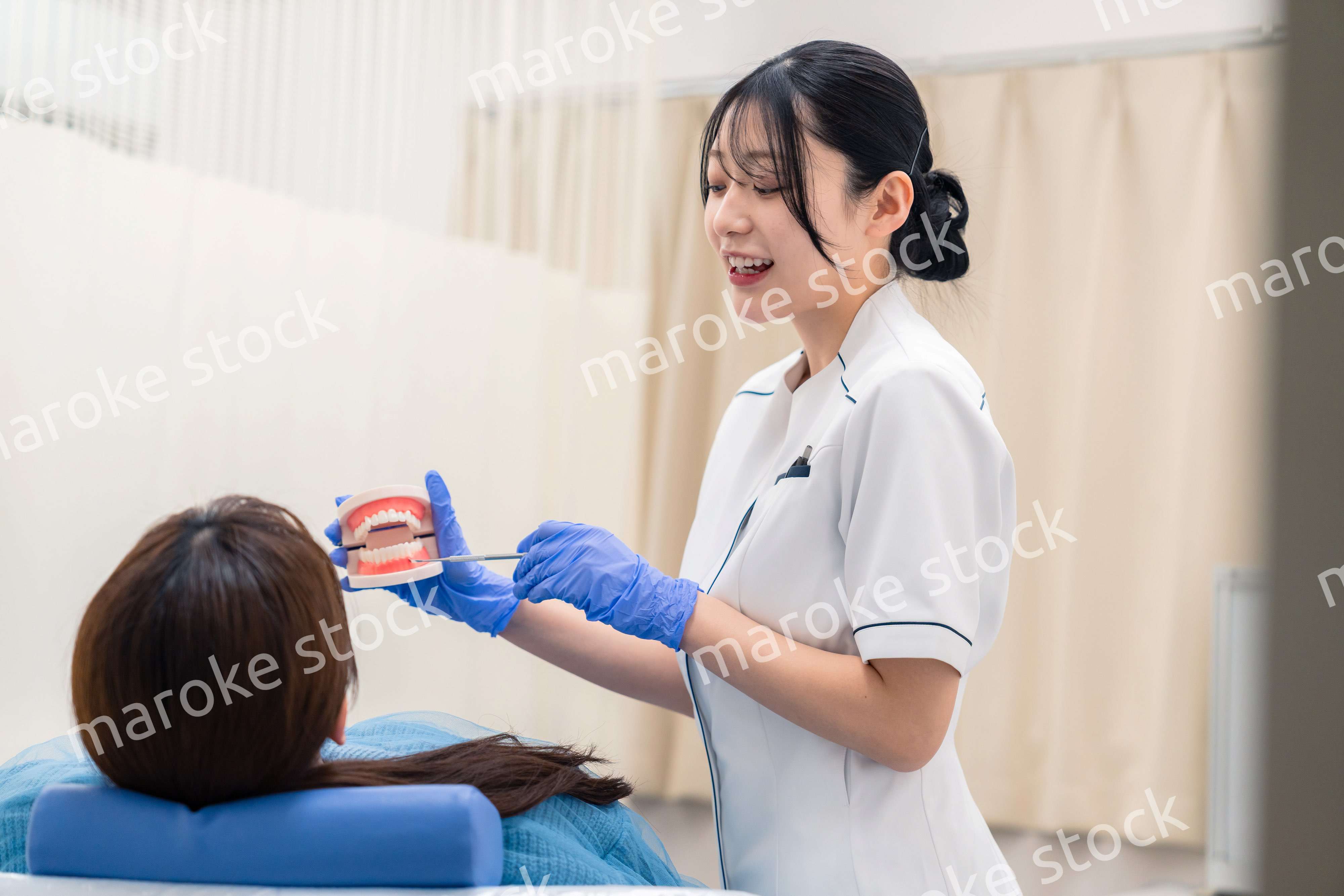 歯の模型を使って患者に説明をする歯科助手の女性