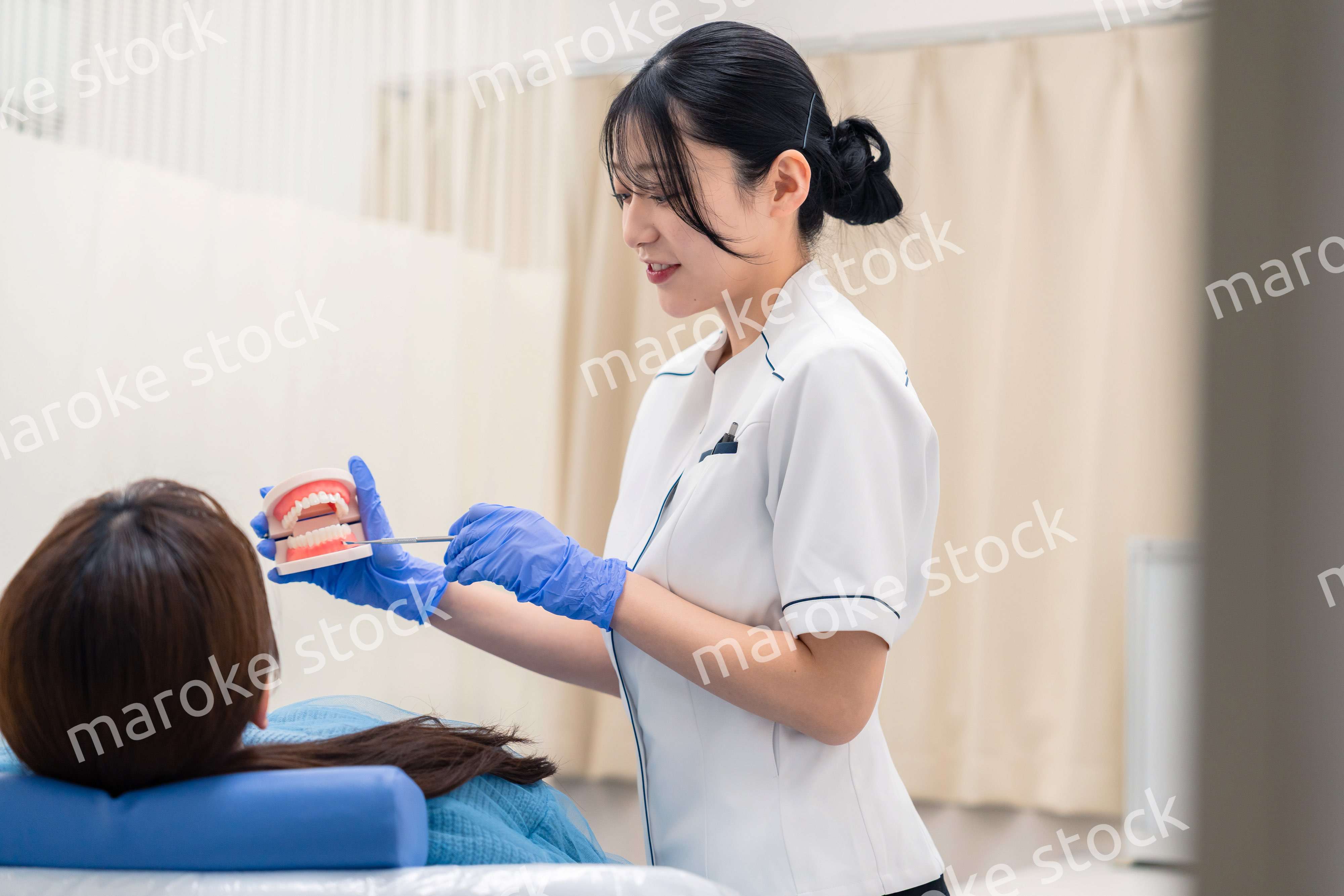 歯の模型を使って患者に説明をする歯科助手の女性