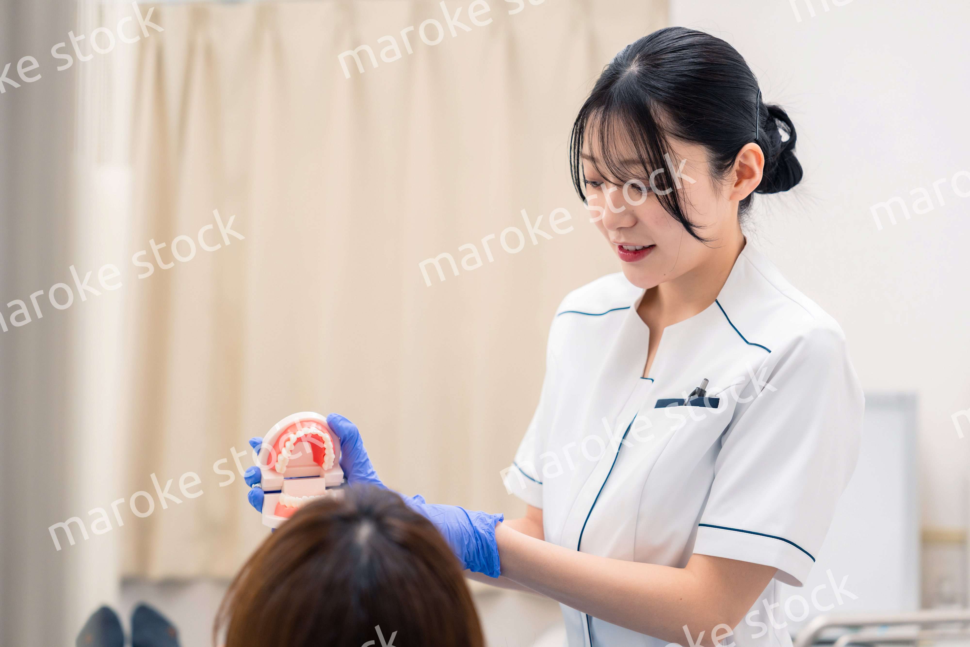 歯の模型を使って患者に説明をする歯科助手の女性