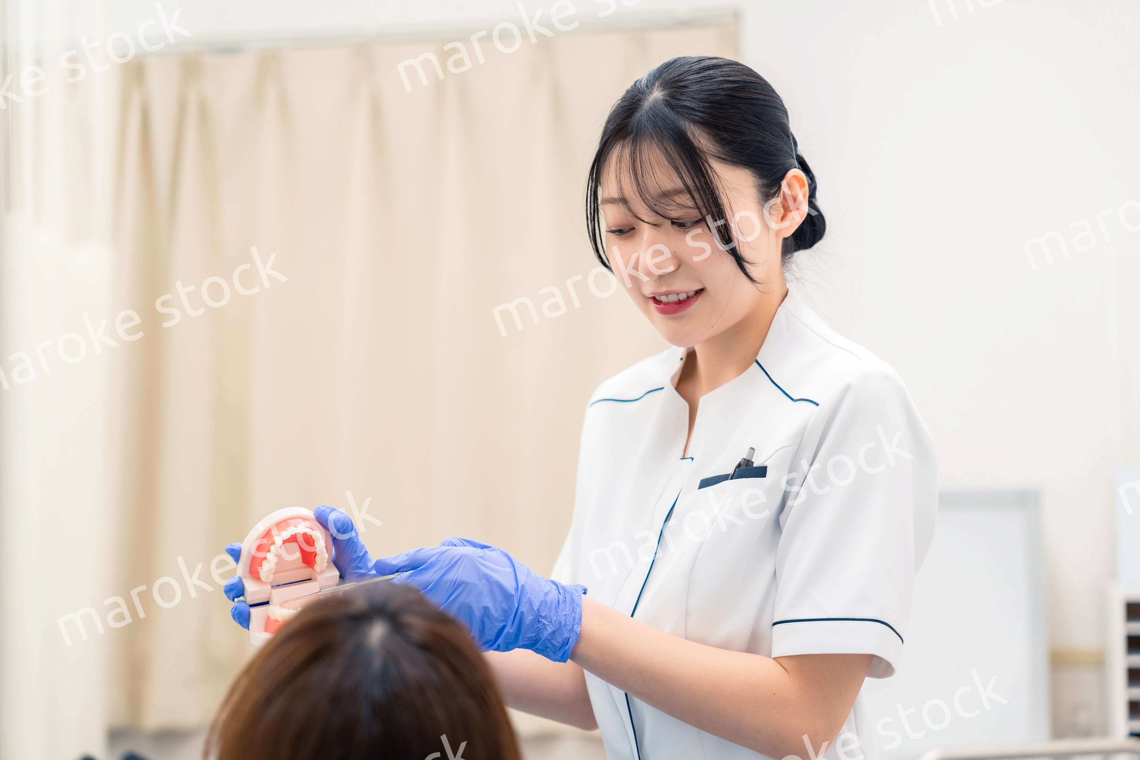 歯の模型を使って患者に説明をする歯科助手の女性
