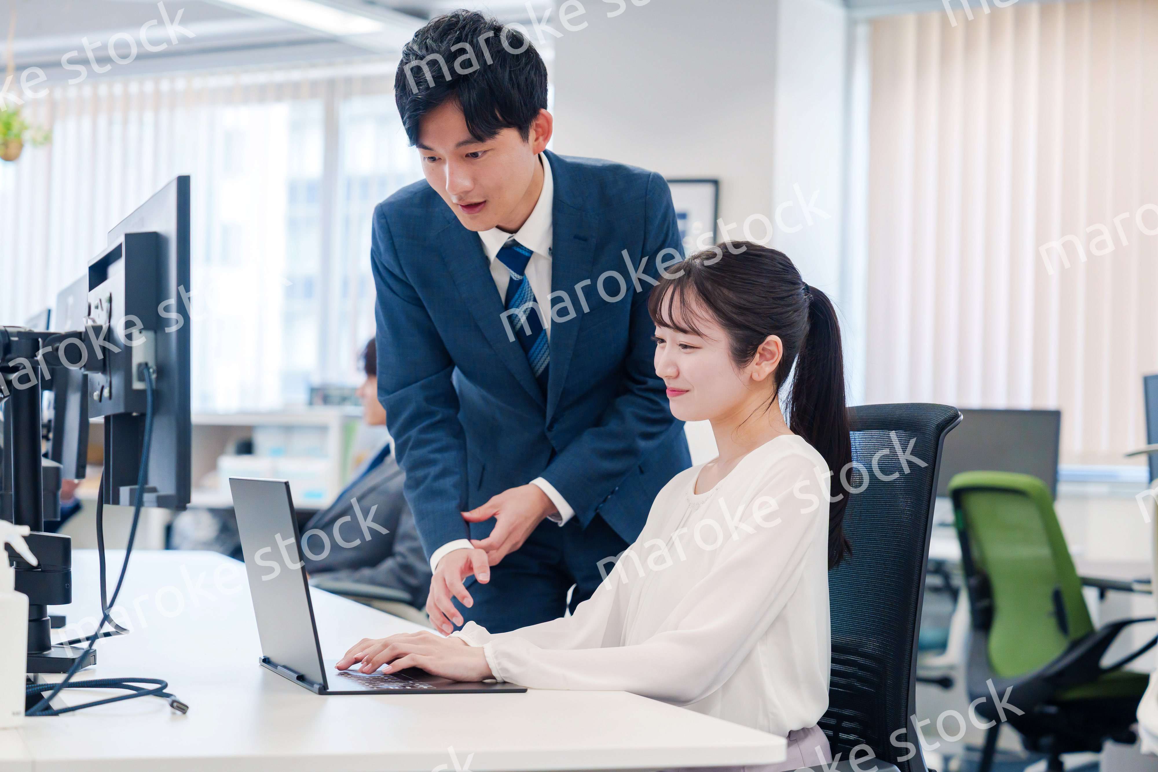 先輩に仕事を教えてもらう若い女性の会社員