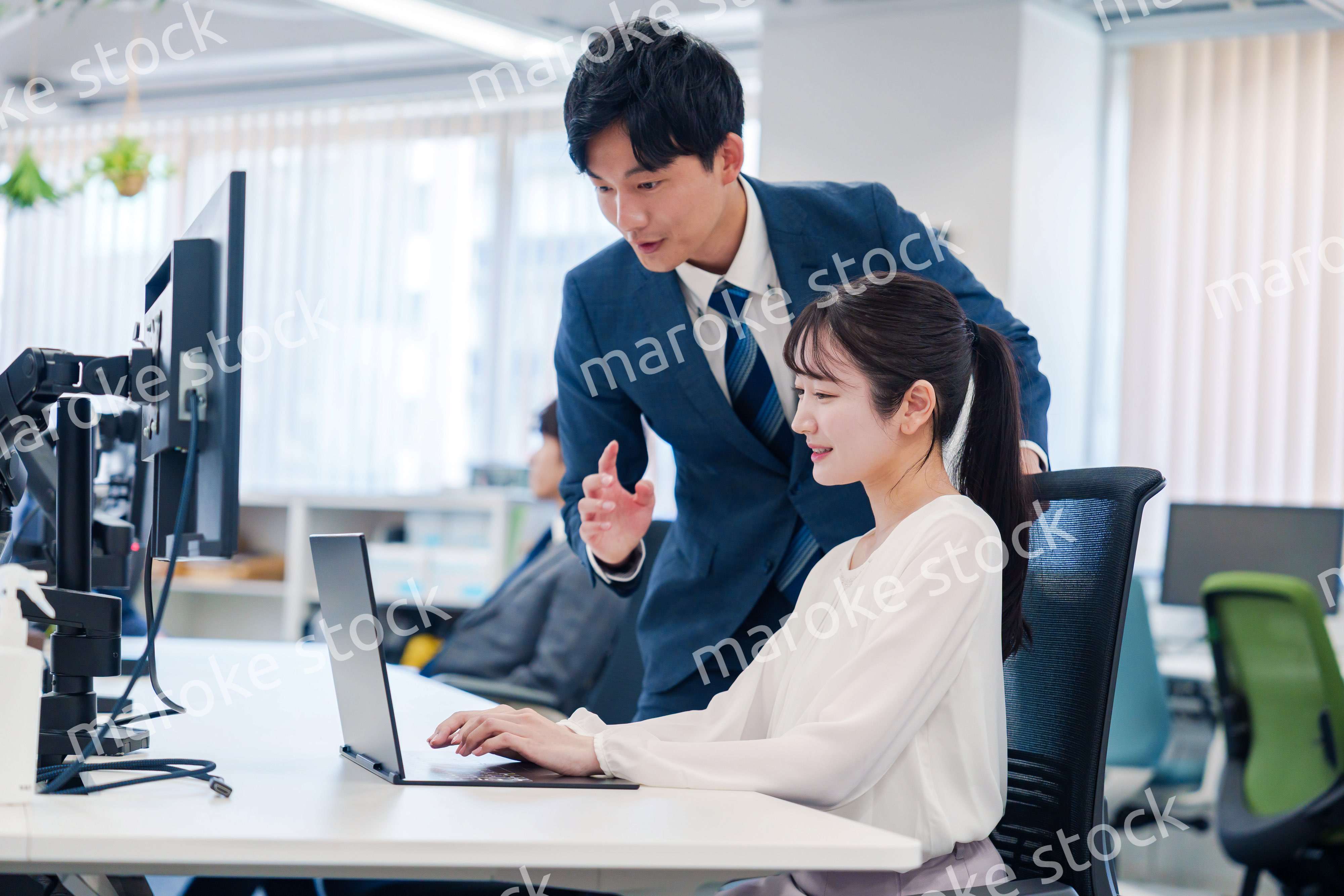 先輩に仕事を教えてもらう若い女性の会社員