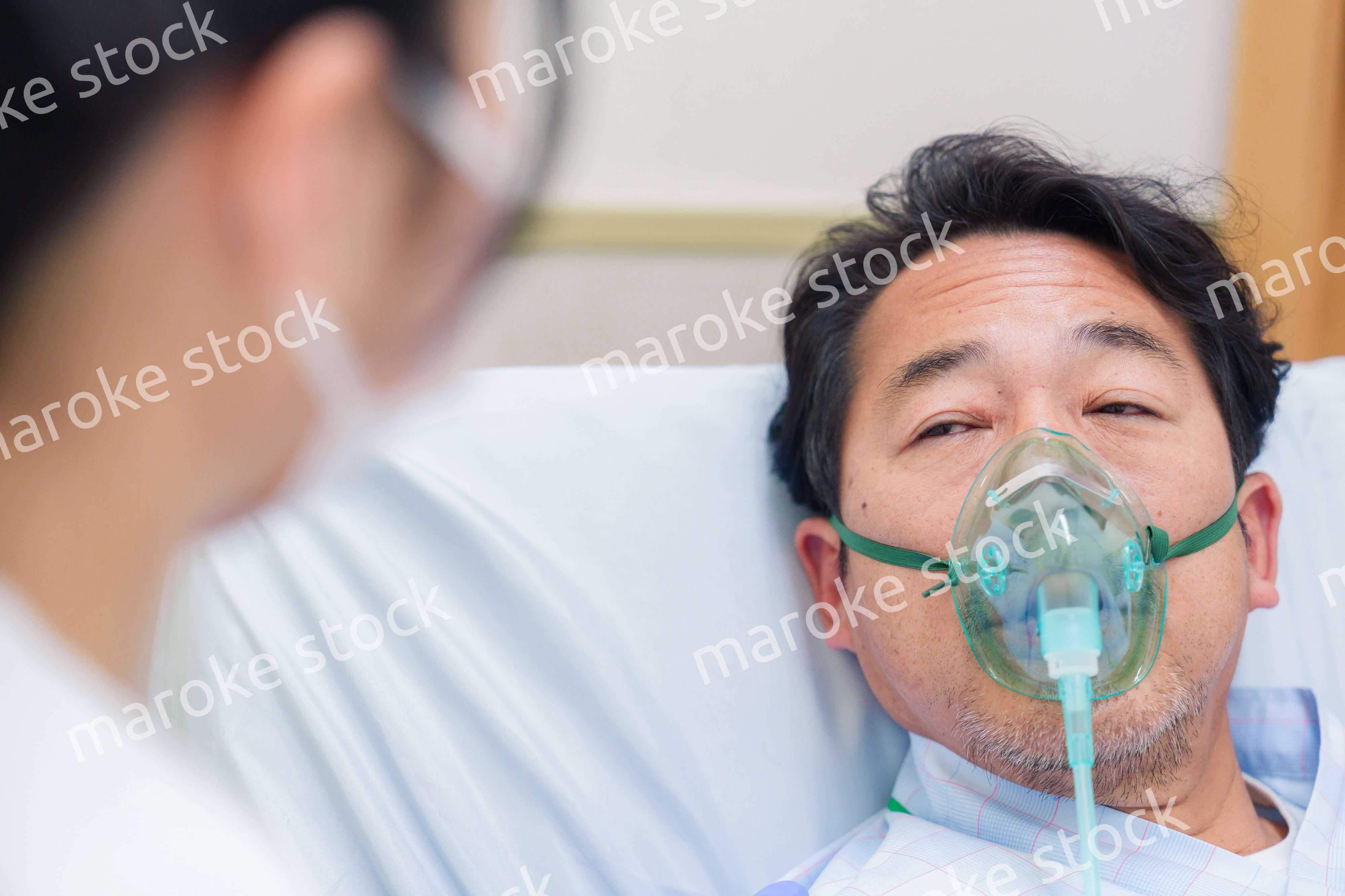 人工呼吸器をつけて話をする入院患者の男性