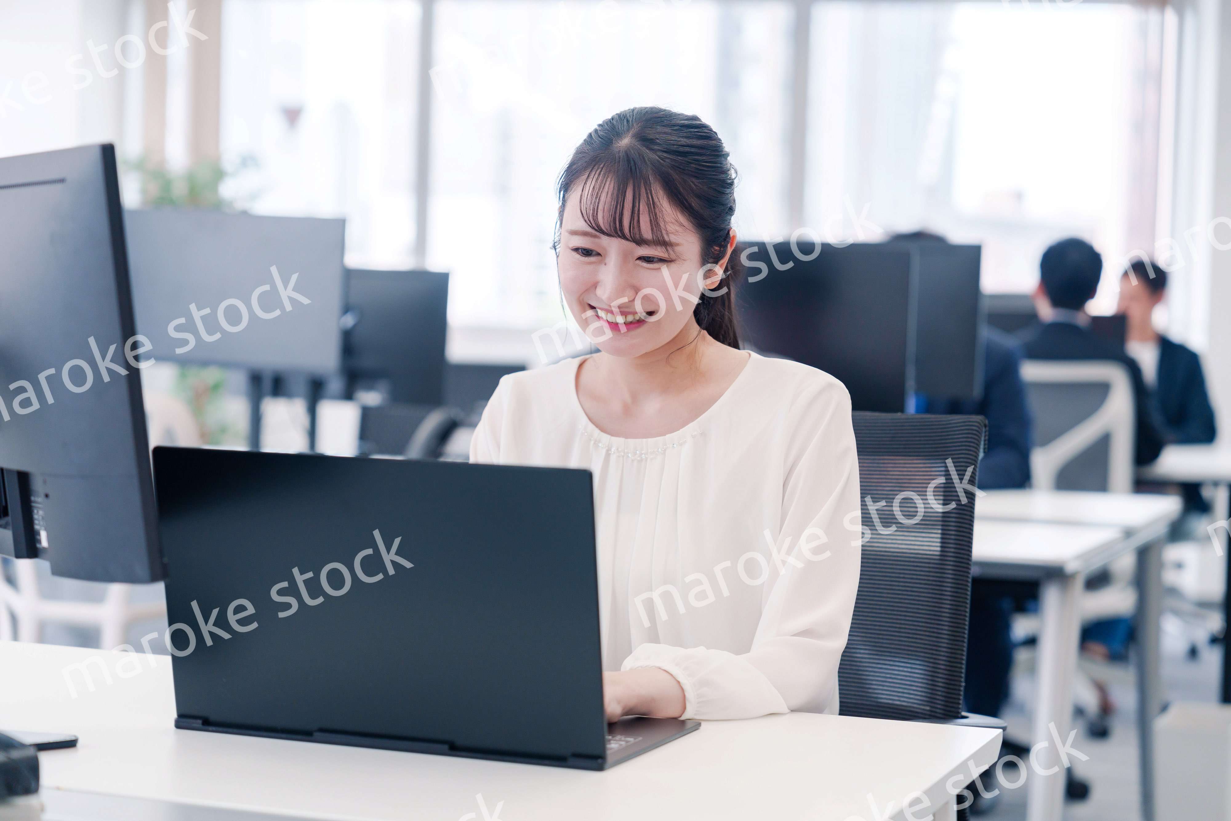 オフィスで笑顔でデスクワークをする若い女性