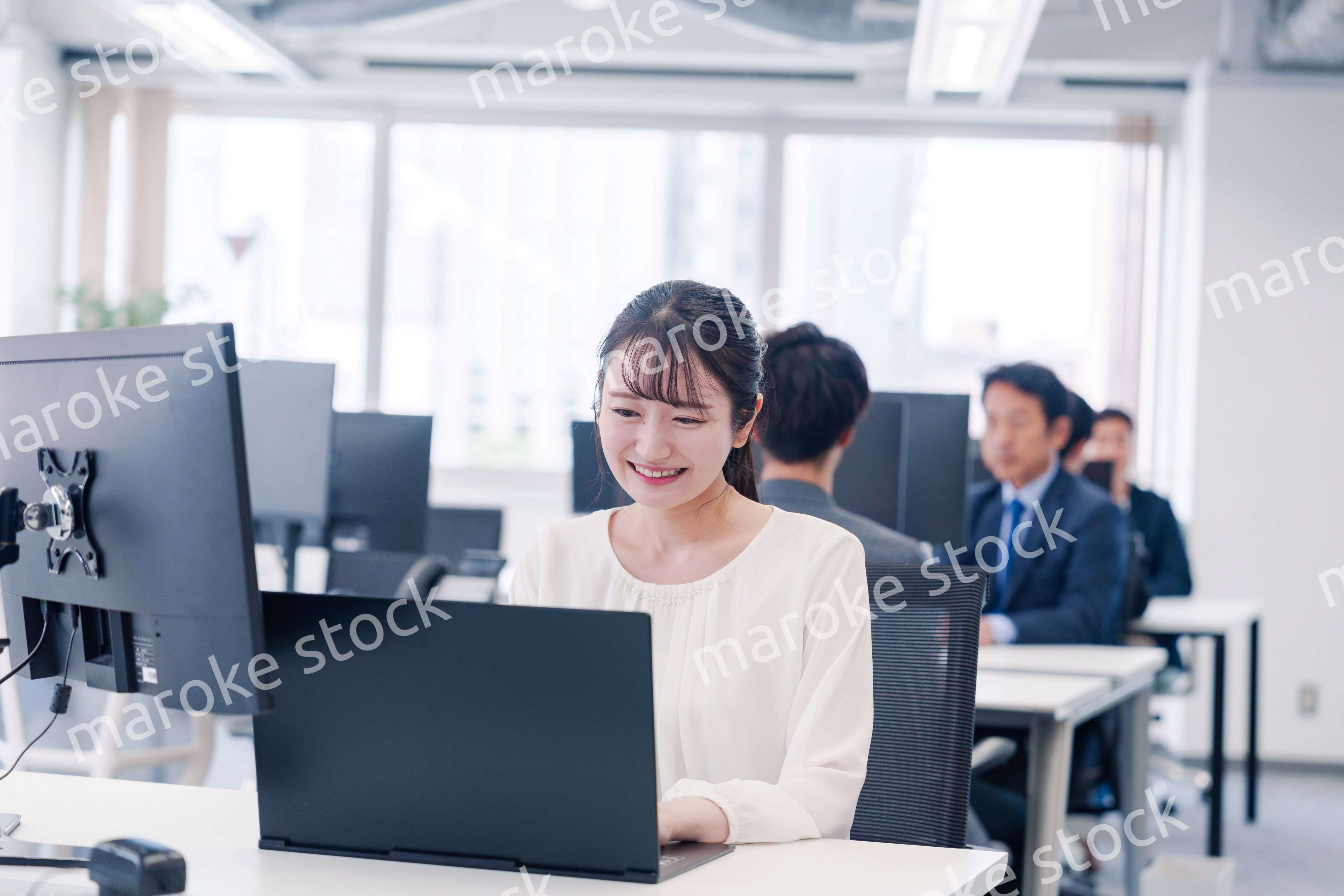 オフィスで笑顔でデスクワークをする若い女性