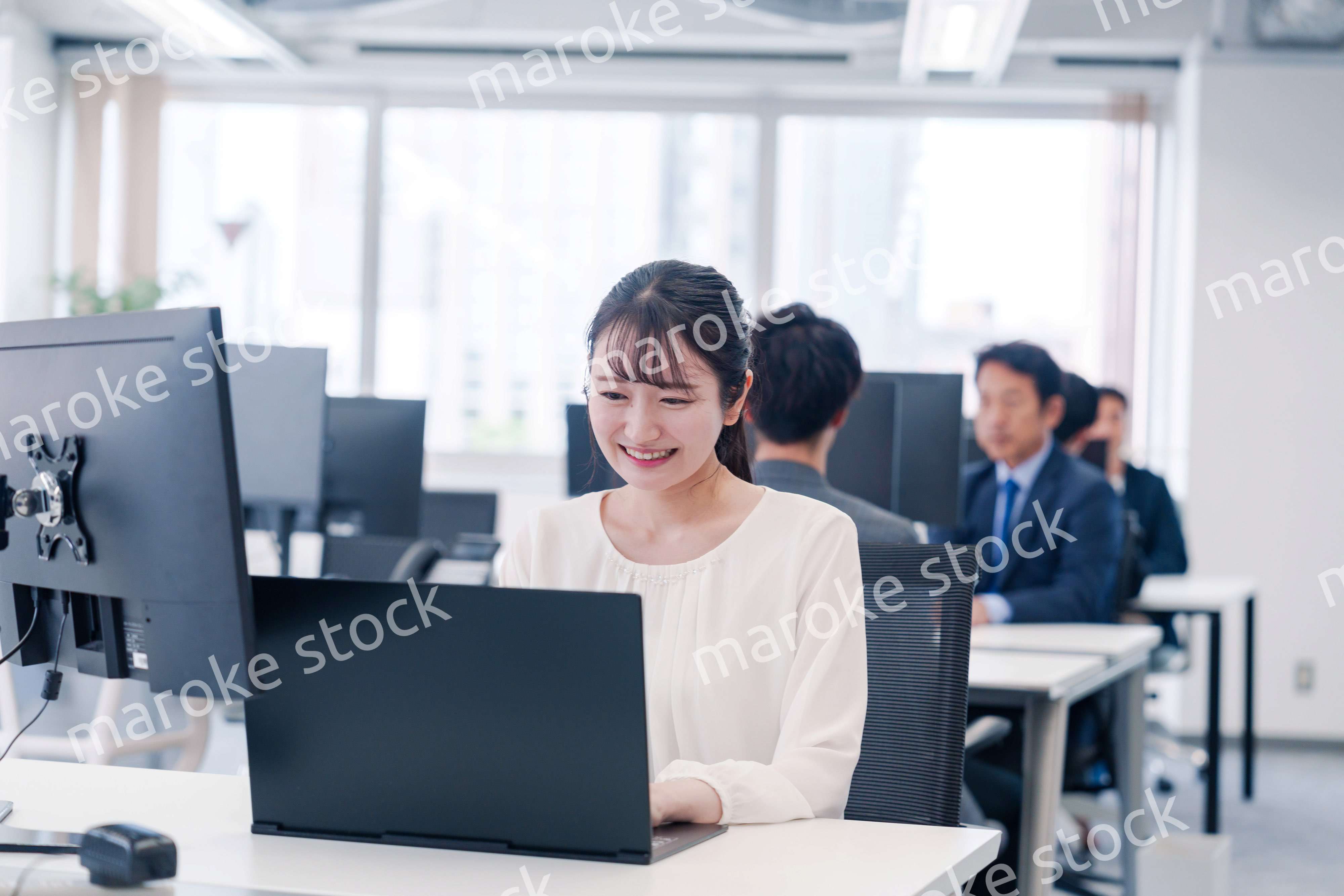 オフィスで笑顔でデスクワークをする若い女性