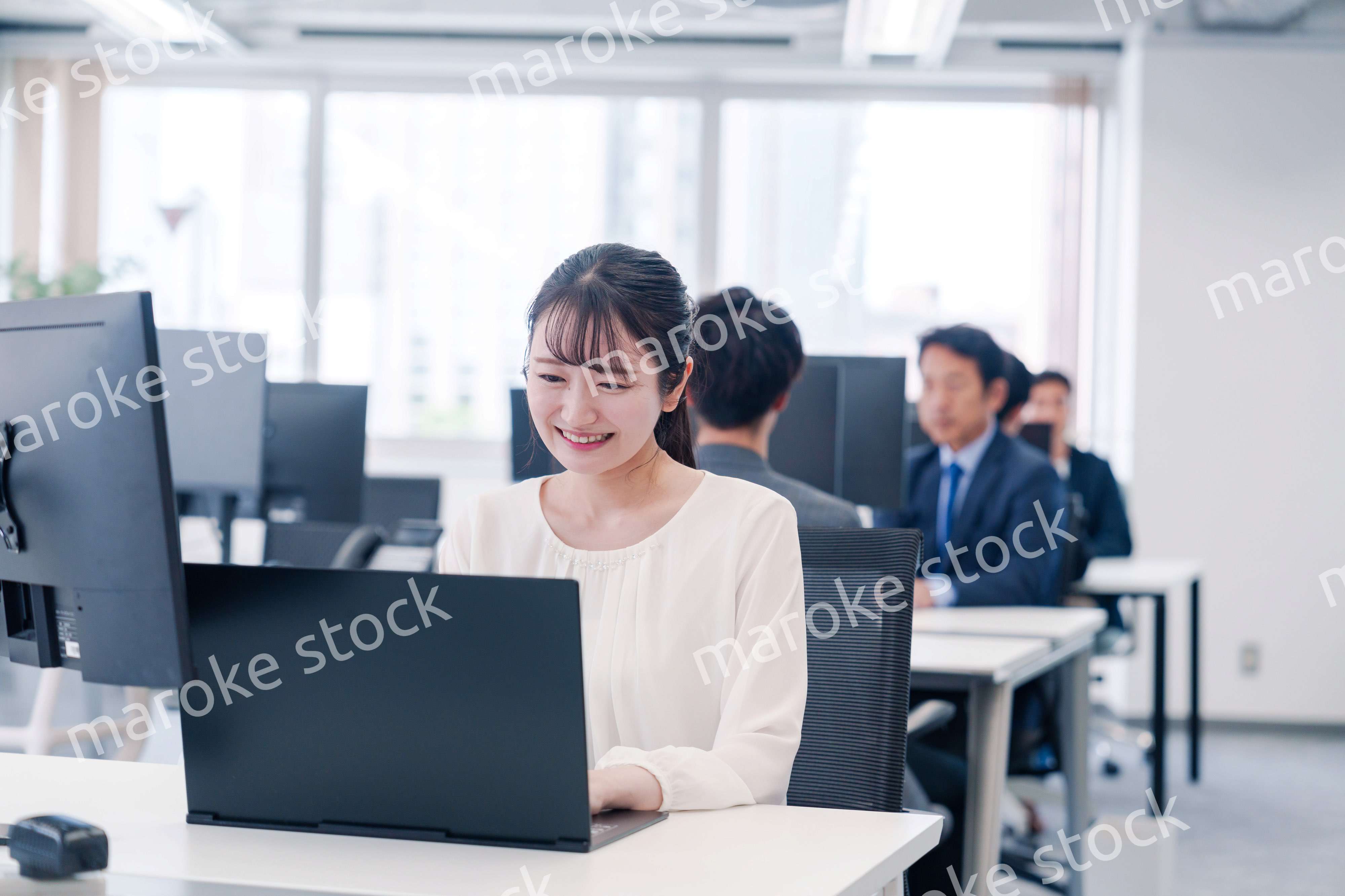 オフィスで笑顔でデスクワークをする若い女性