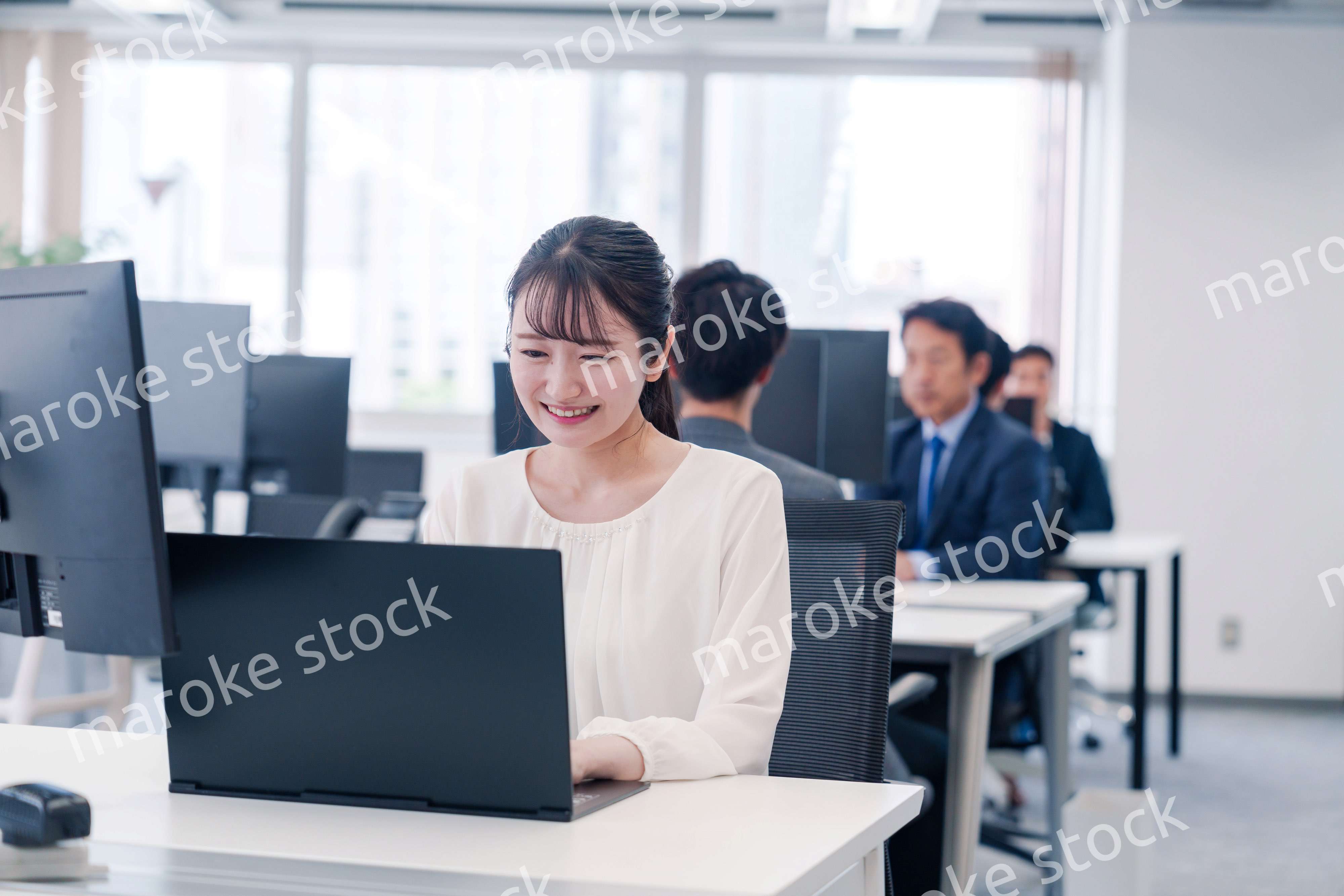 オフィスで笑顔でデスクワークをする若い女性