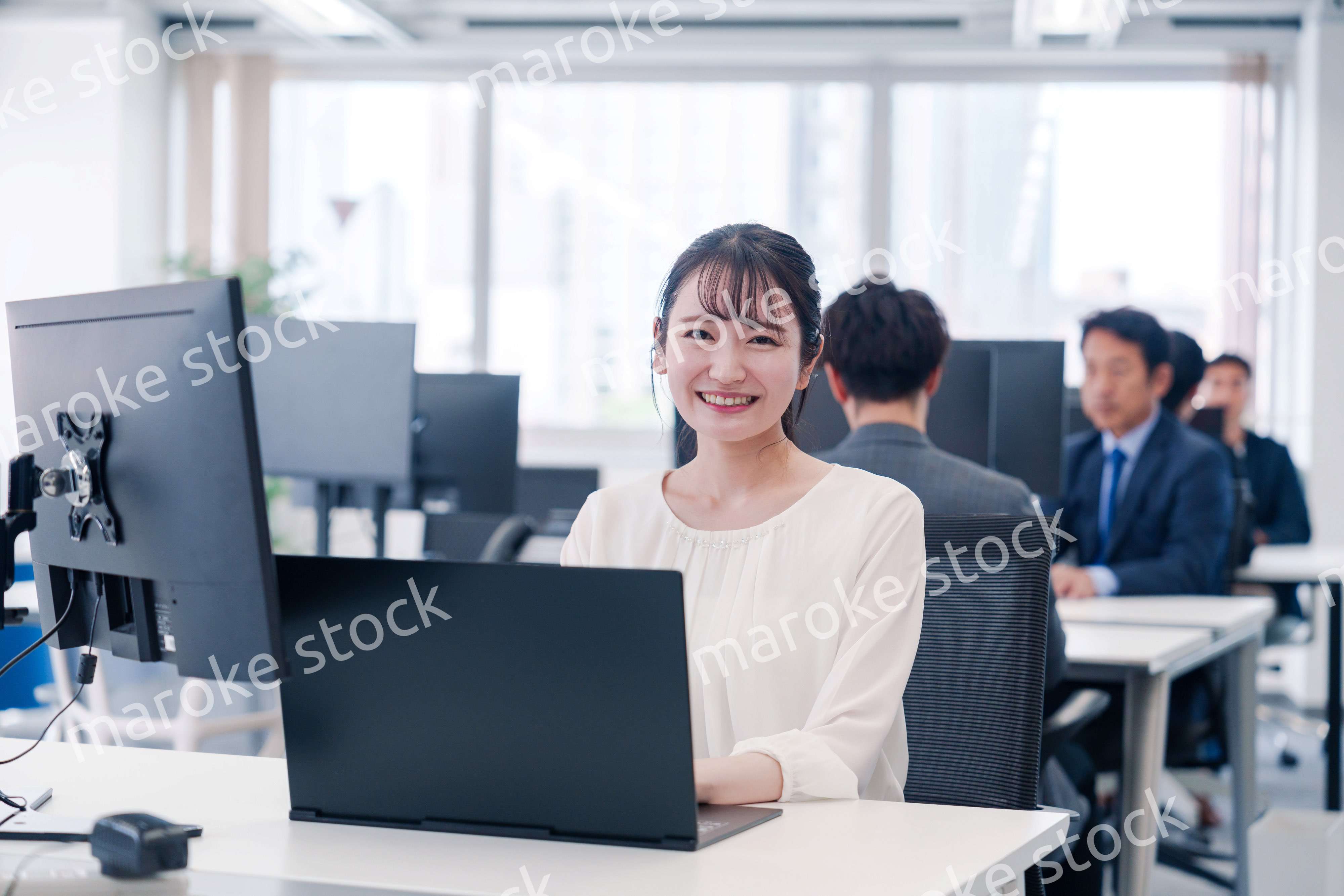 オフィスで笑顔でデスクワークをする若い女性