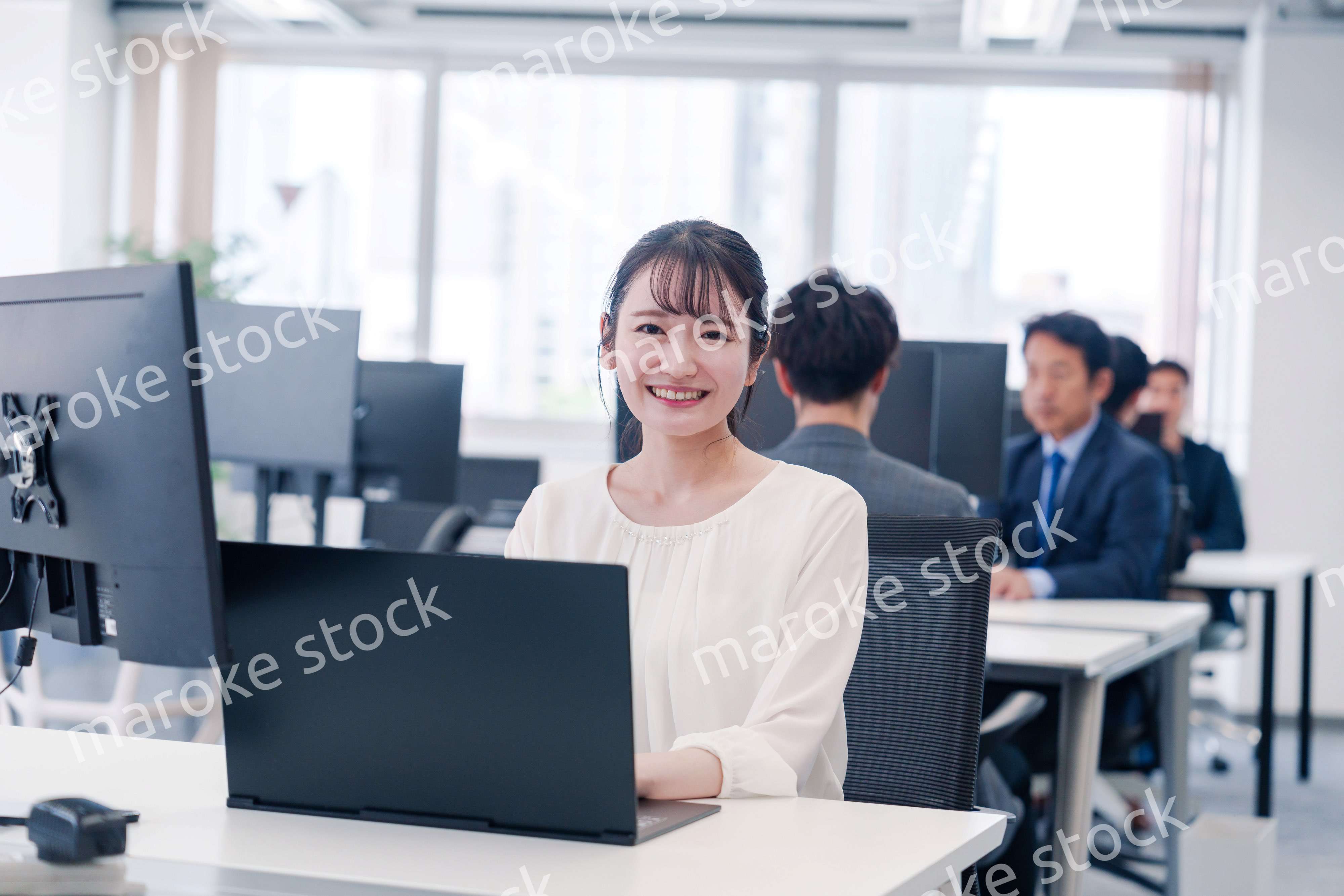 オフィスで笑顔でデスクワークをする若い女性