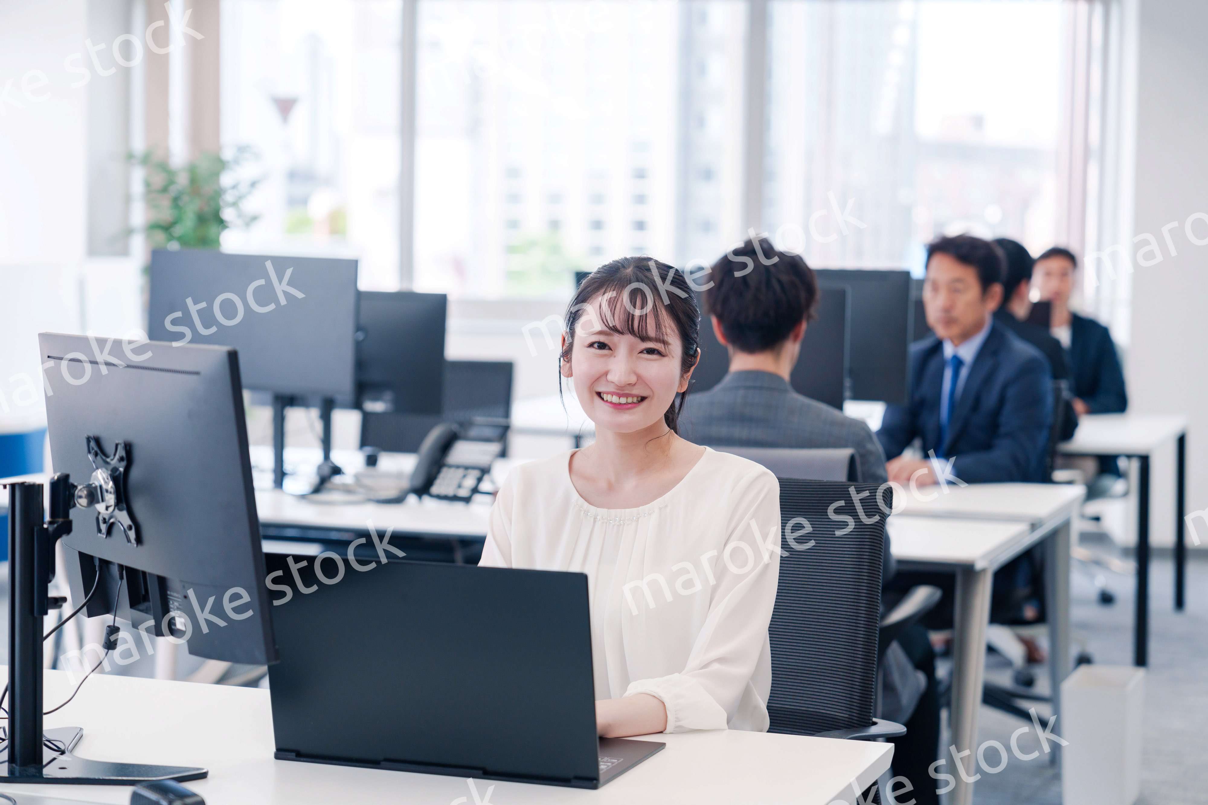 オフィスで笑顔でデスクワークをする若い女性