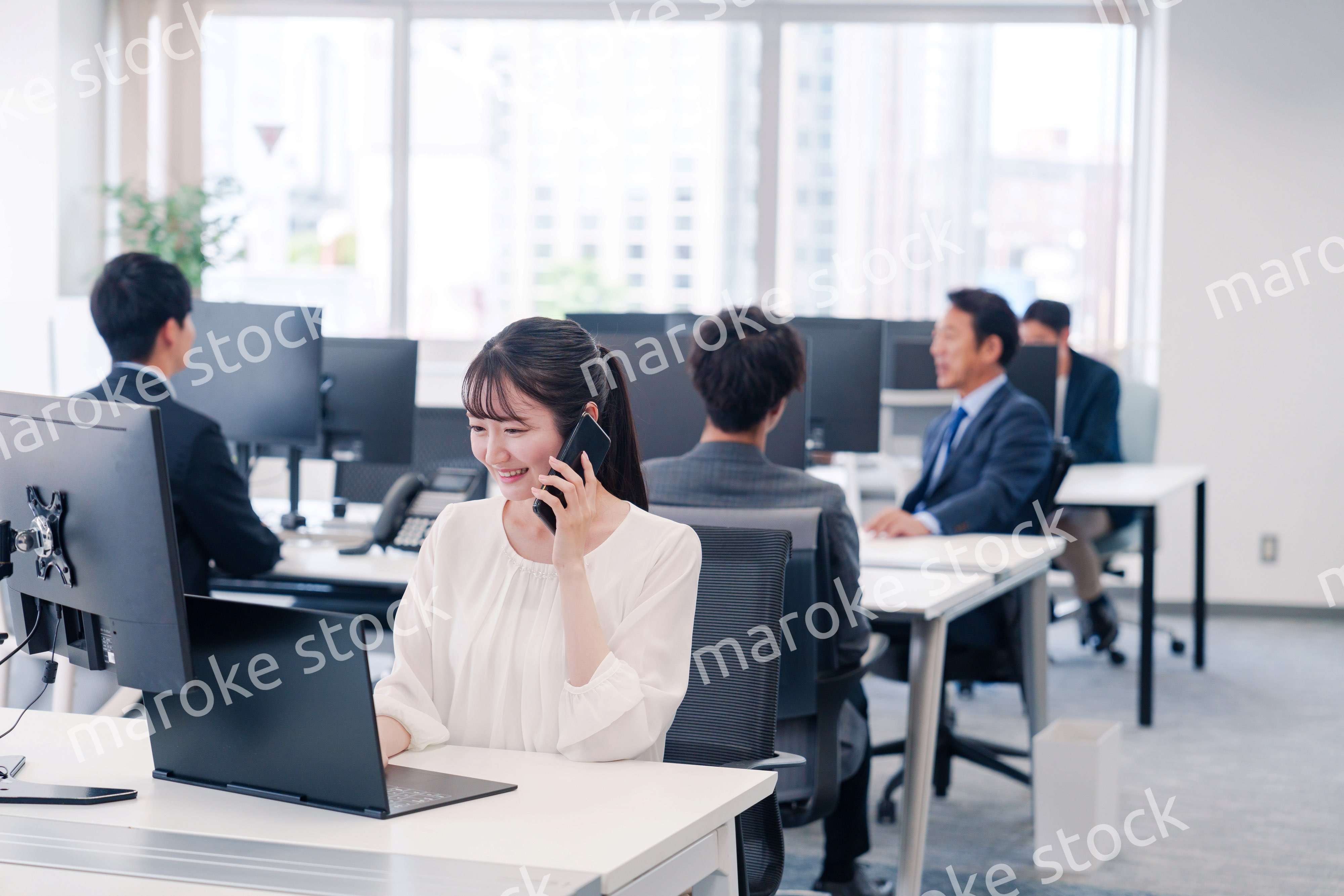 オフィスの中でスマホで通話をするビジネスパーソン