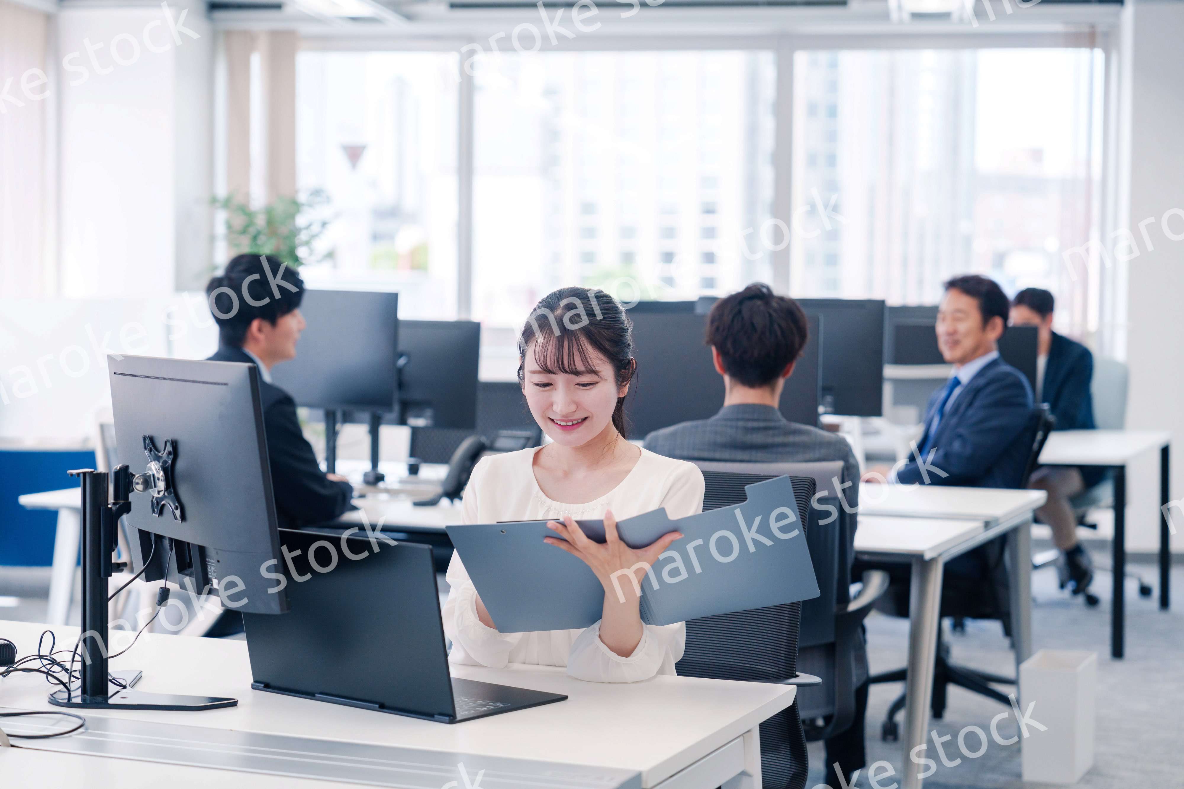 オフィスで笑顔でデスクワークをする若い女性