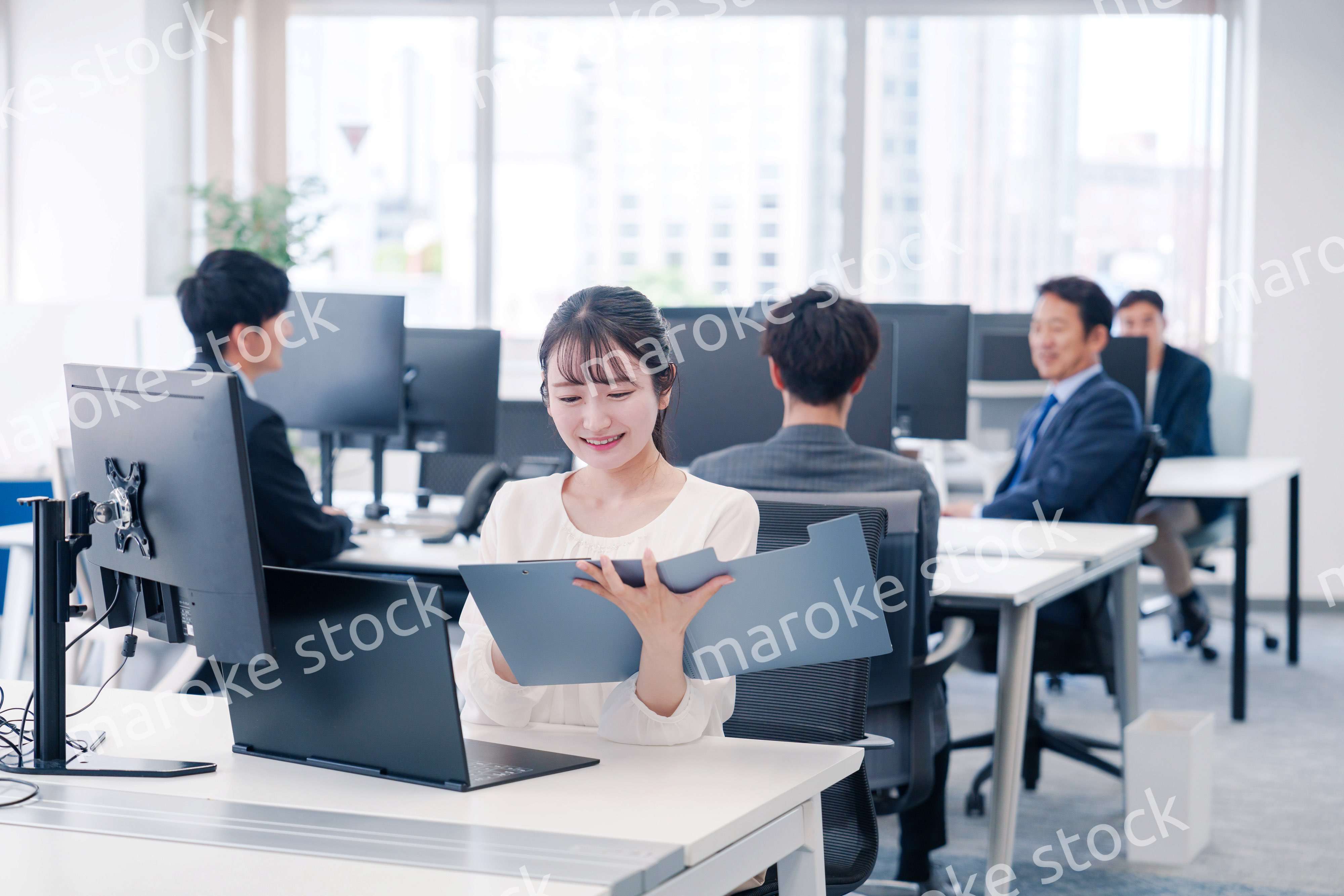 オフィスで笑顔でデスクワークをする若い女性