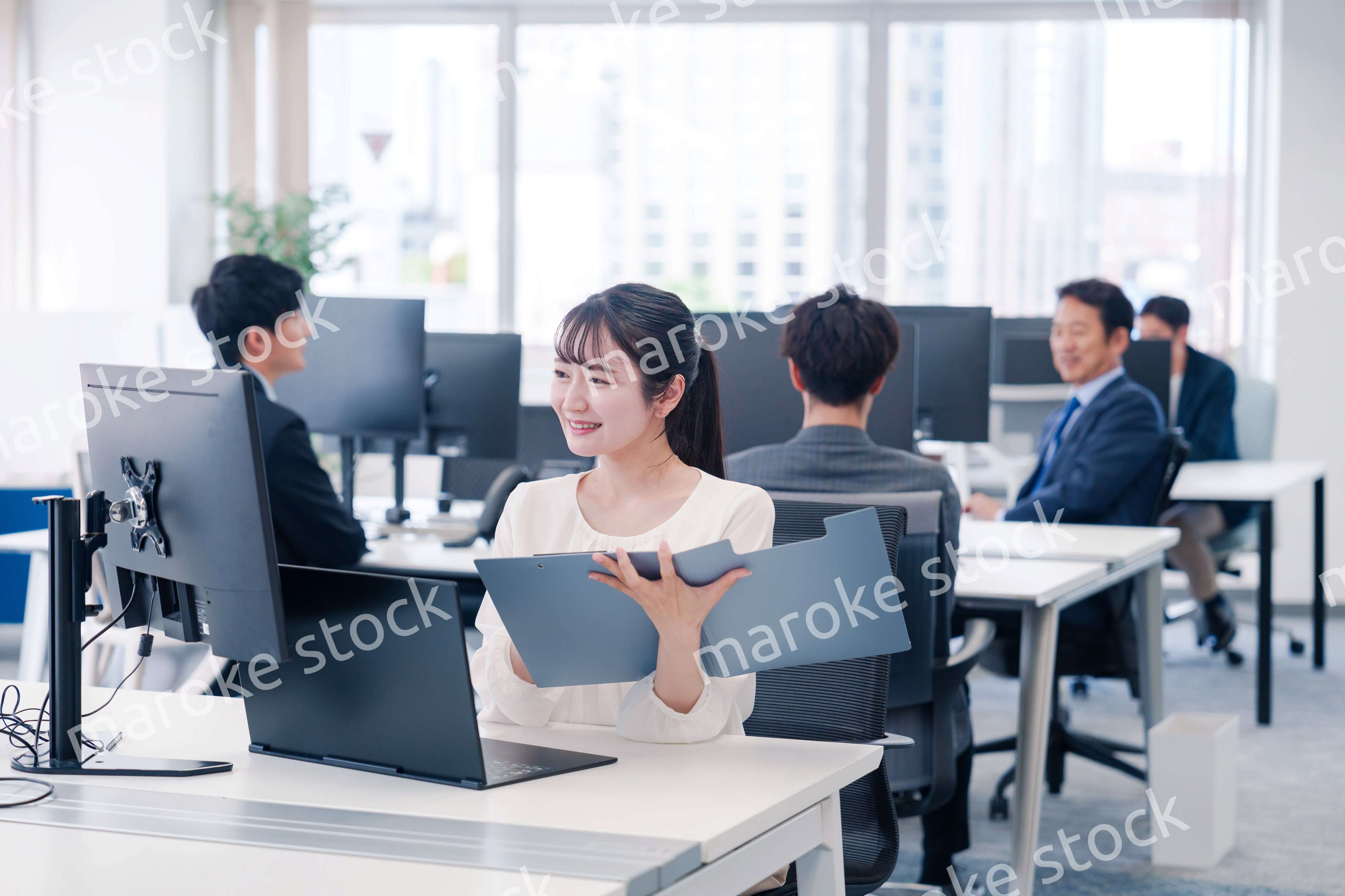 オフィスで笑顔でデスクワークをする若い女性