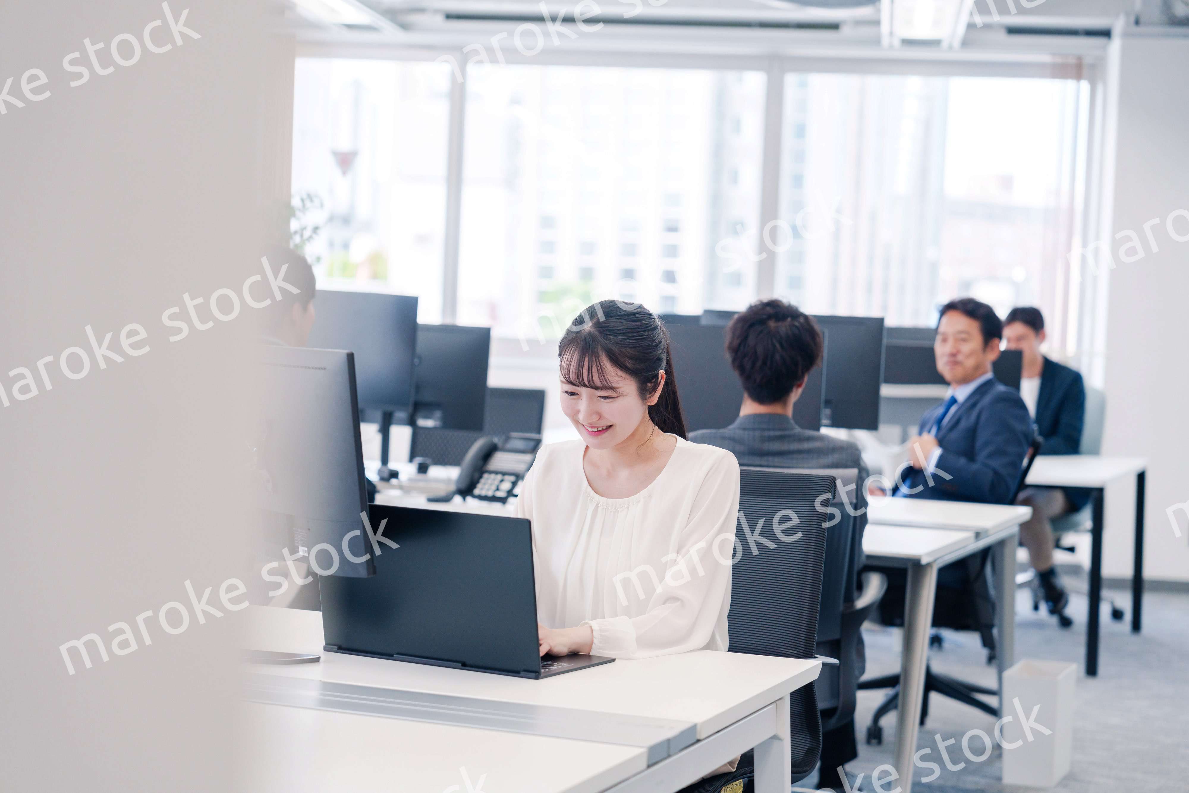 オフィスで笑顔でデスクワークをする若い女性