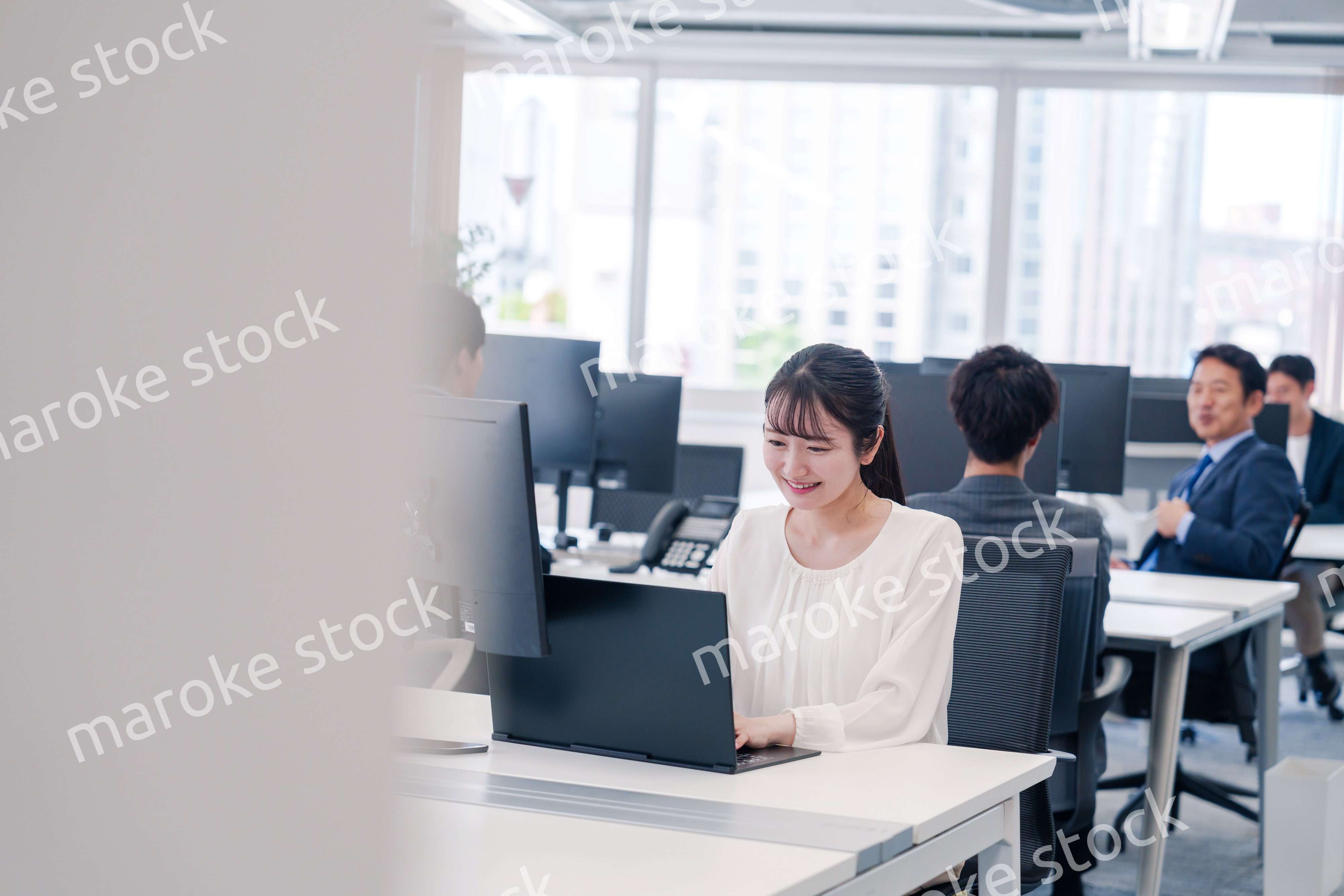 オフィスで笑顔でデスクワークをする若い女性