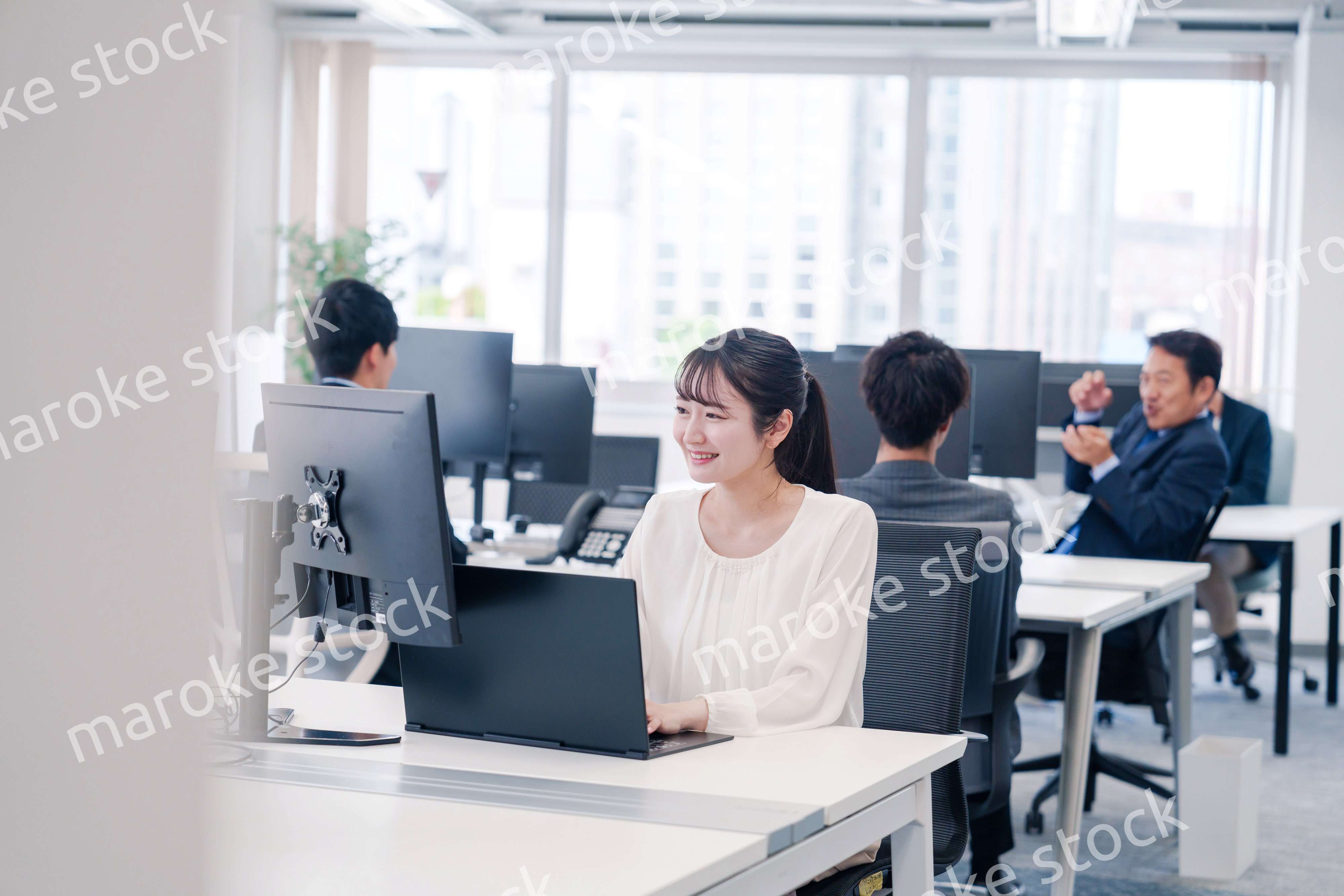 オフィスで笑顔でデスクワークをする若い女性