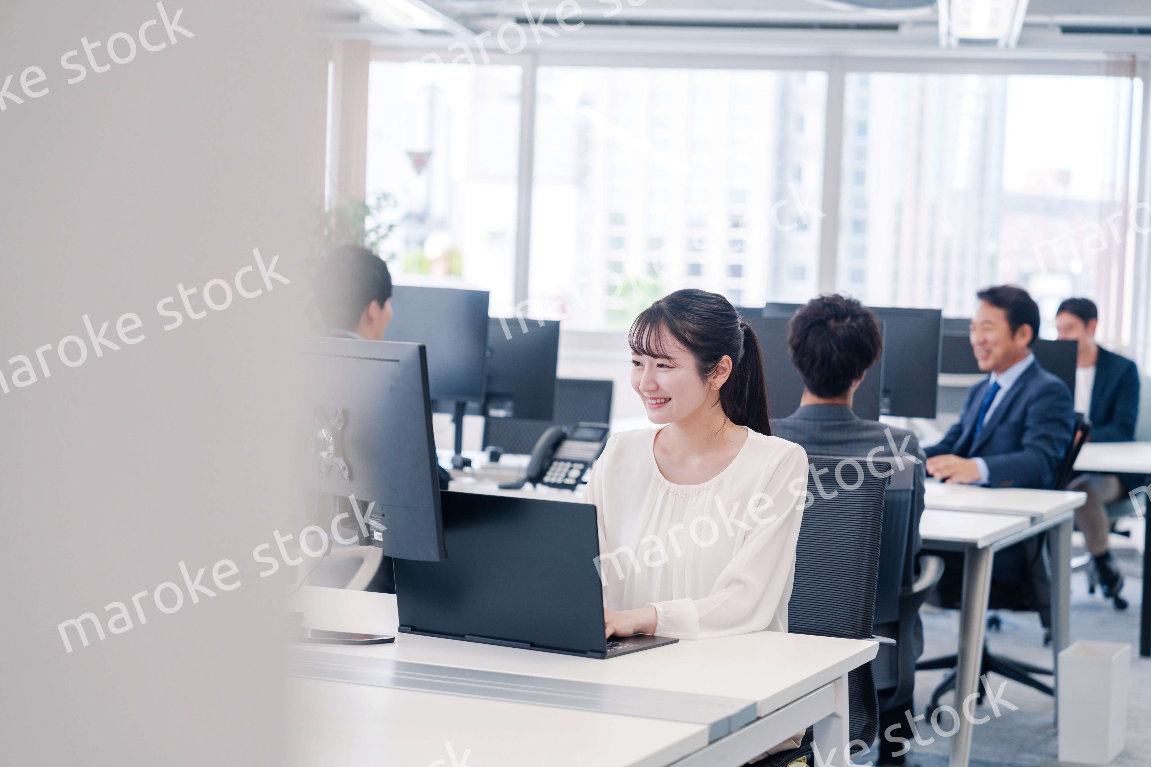 オフィスで笑顔でデスクワークをする若い女性