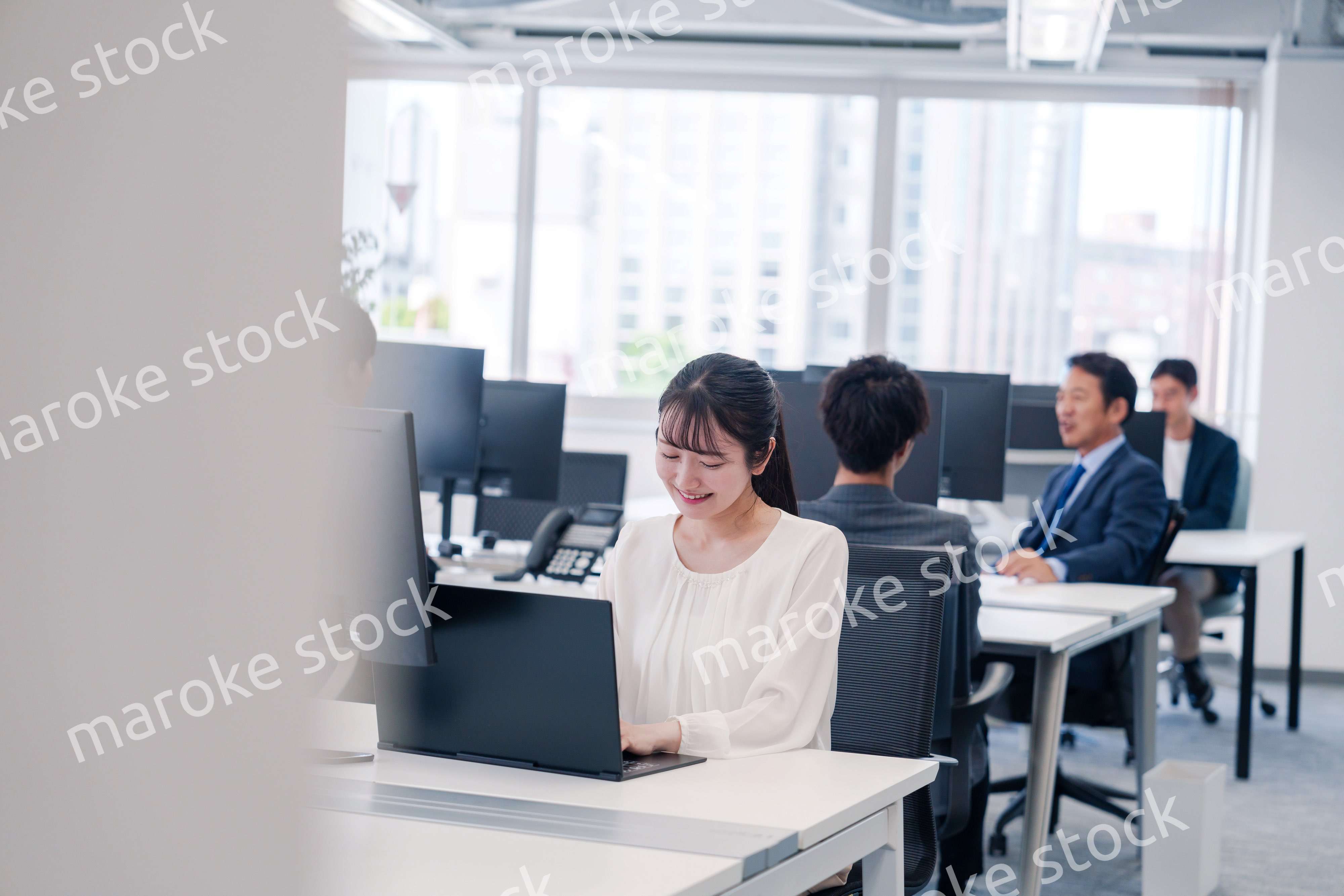 オフィスで笑顔でデスクワークをする若い女性