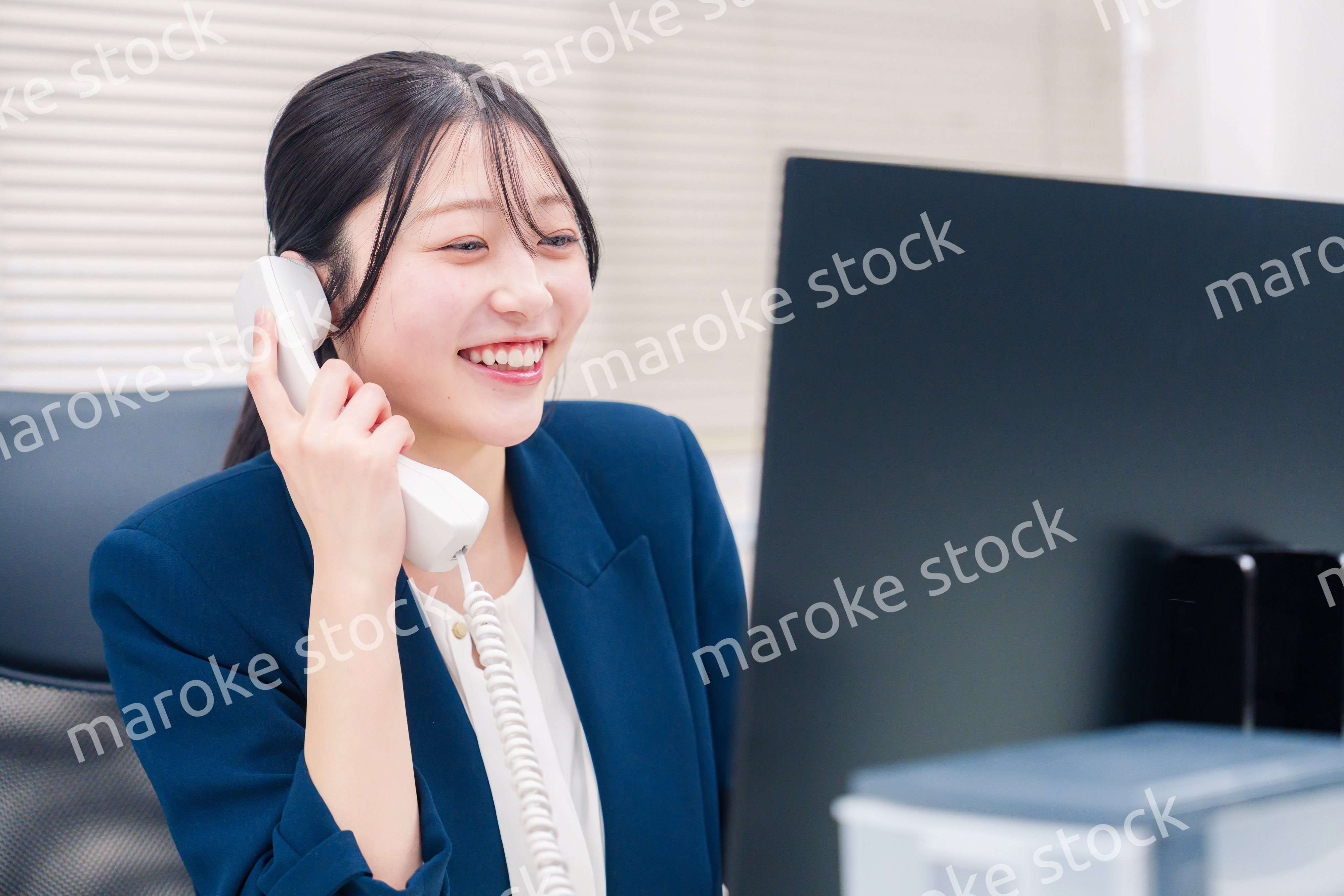 オフィスの固定電話で通話をする女性ビジネスパーソン