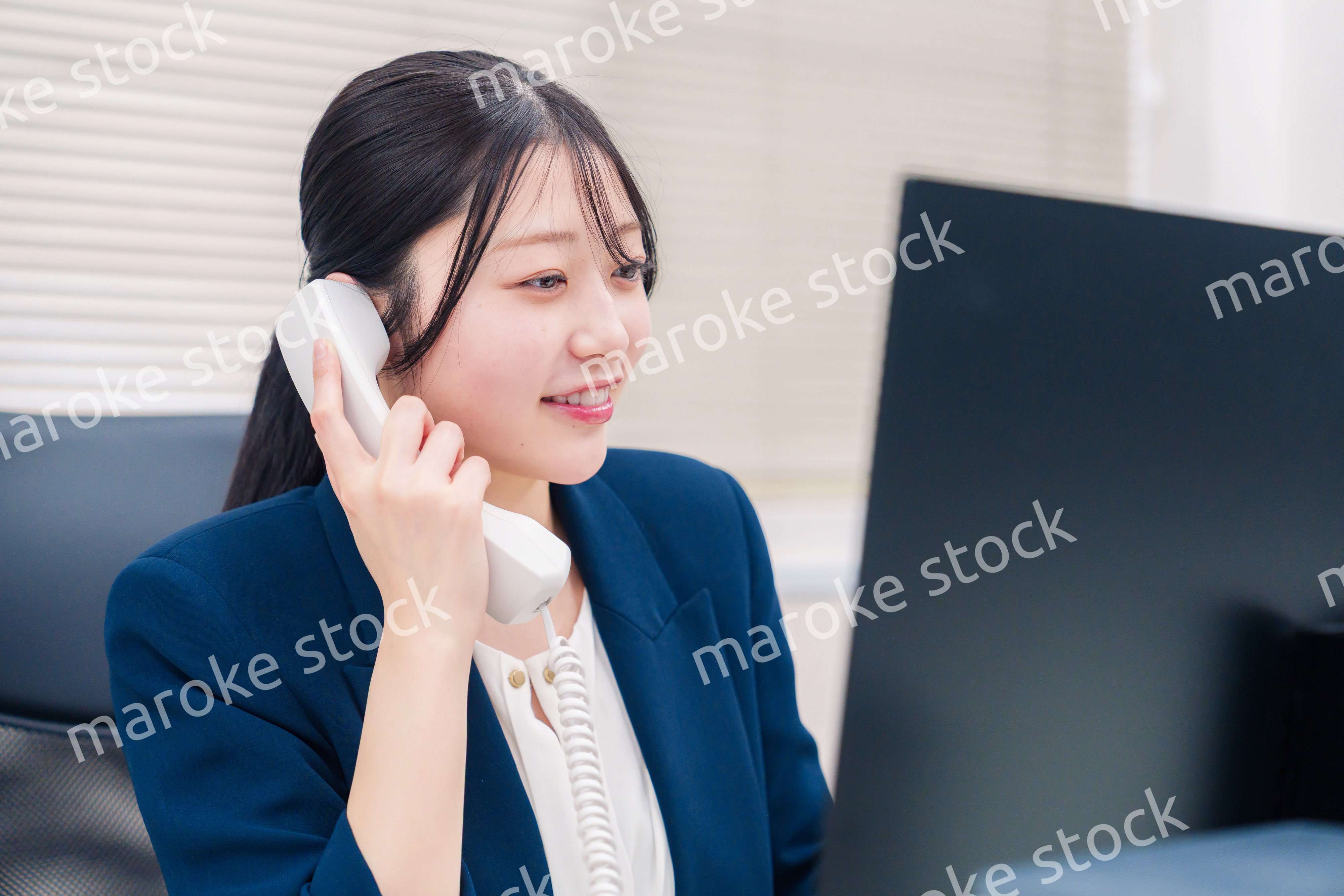 オフィスの固定電話で通話をする女性ビジネスパーソン