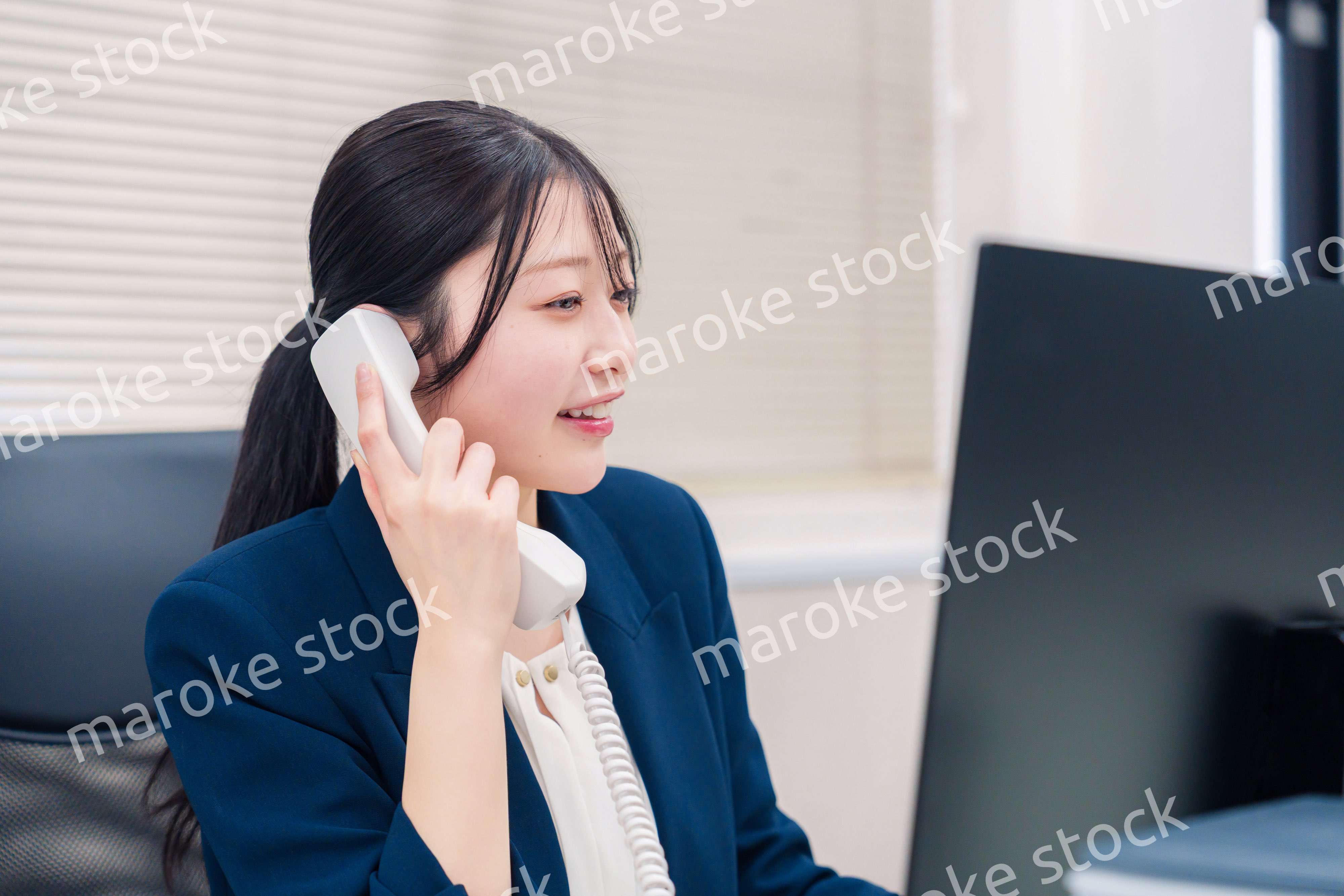 オフィスの固定電話で通話をする女性ビジネスパーソン