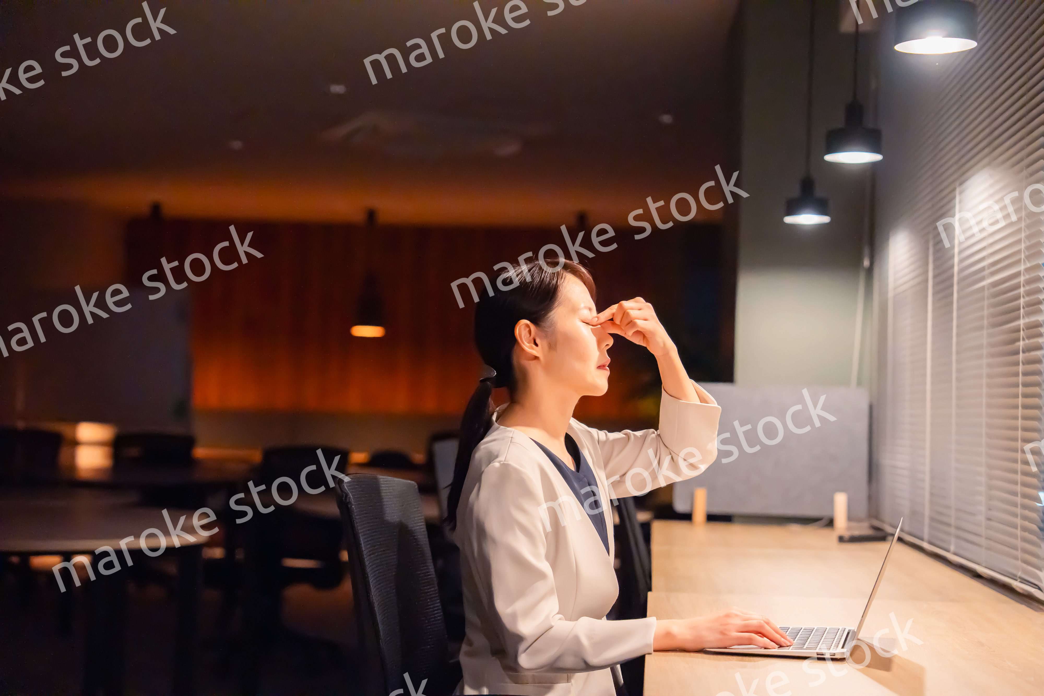 オフィスで暗くなるまで残業をして疲れる女性管理職