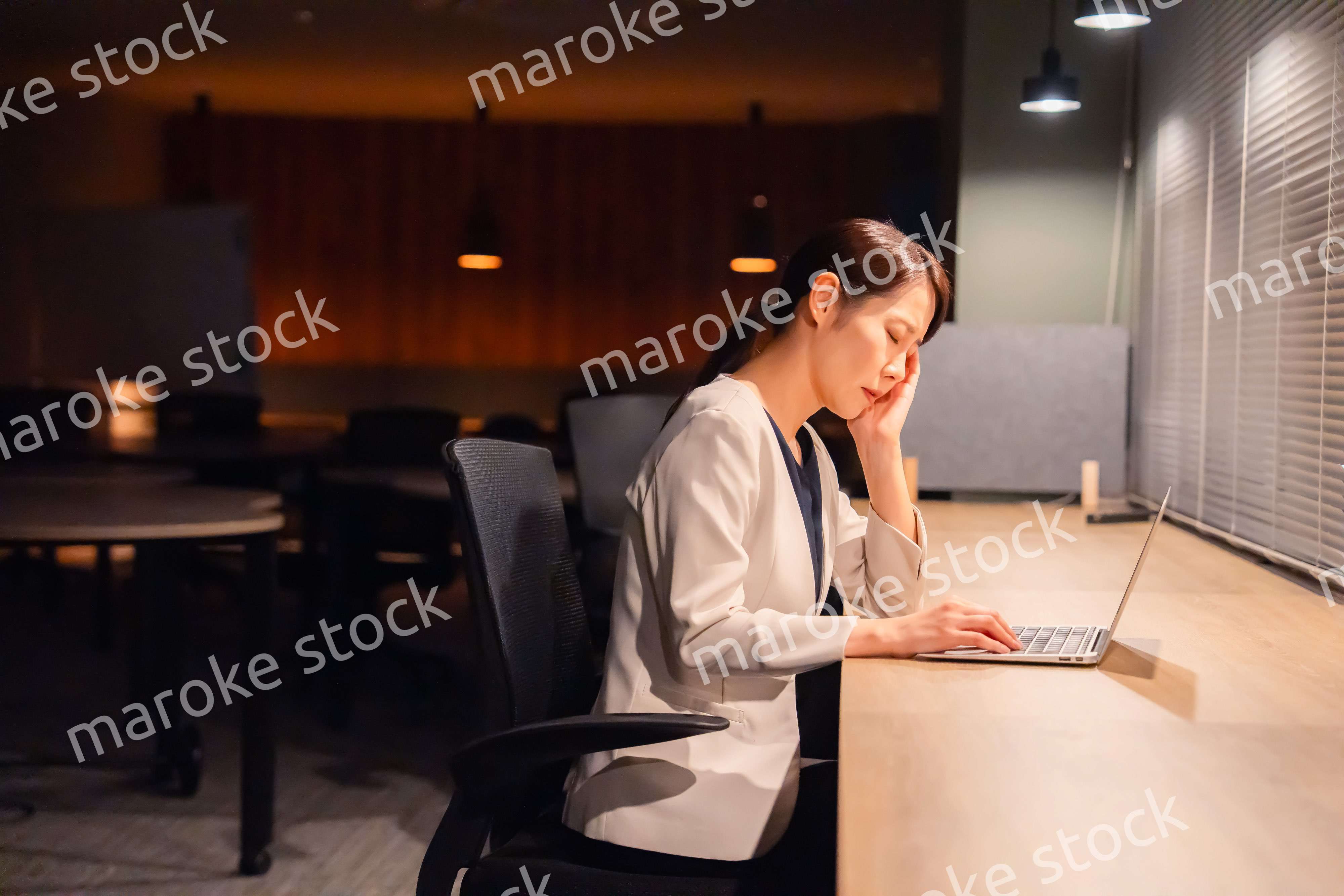 オフィスで暗くなるまで残業をして疲れる女性管理職